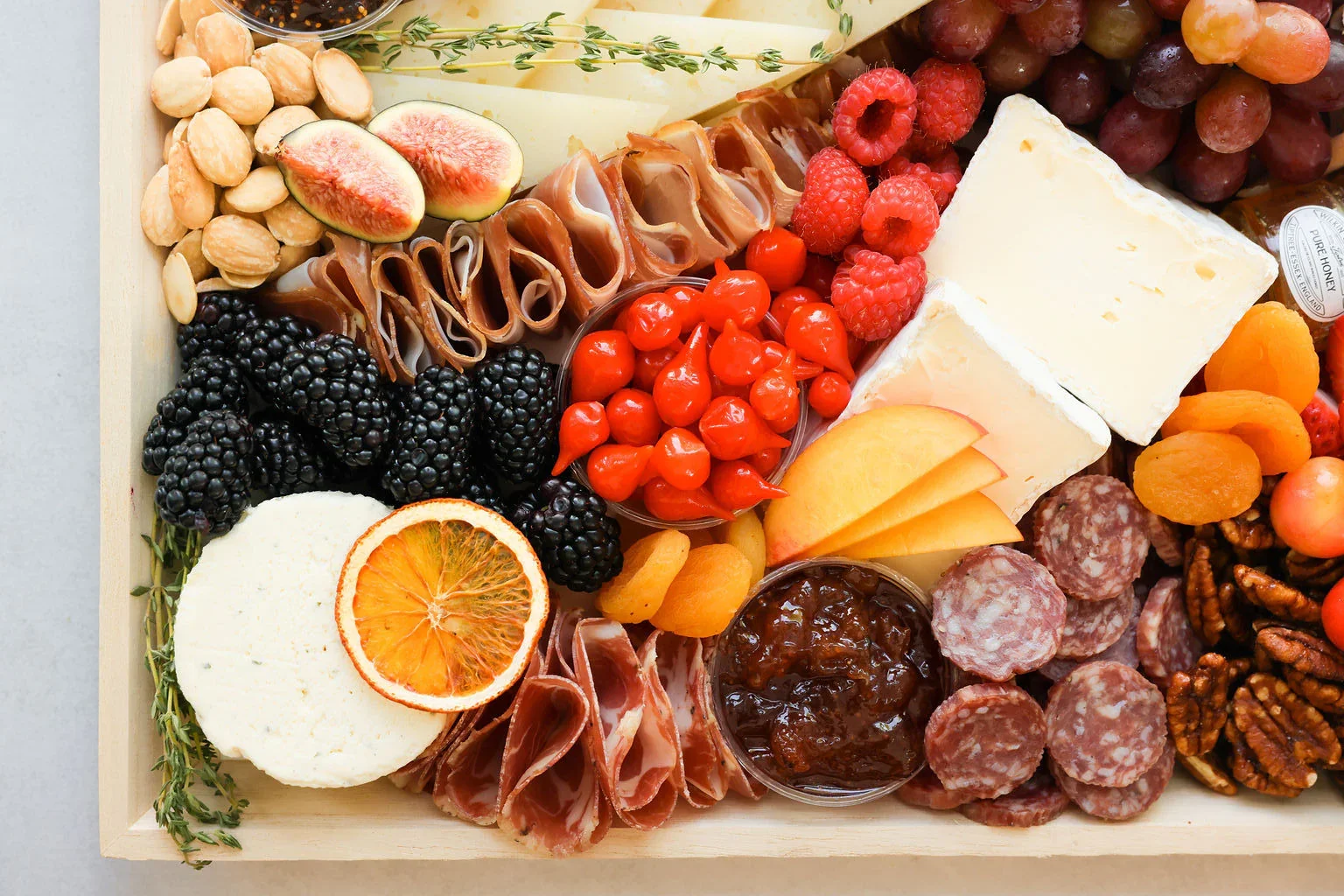 Charcuterie board with assorted cheeses, grapes, berries, figs, nuts, cured meats, dried fruits, and a small jar of jam.