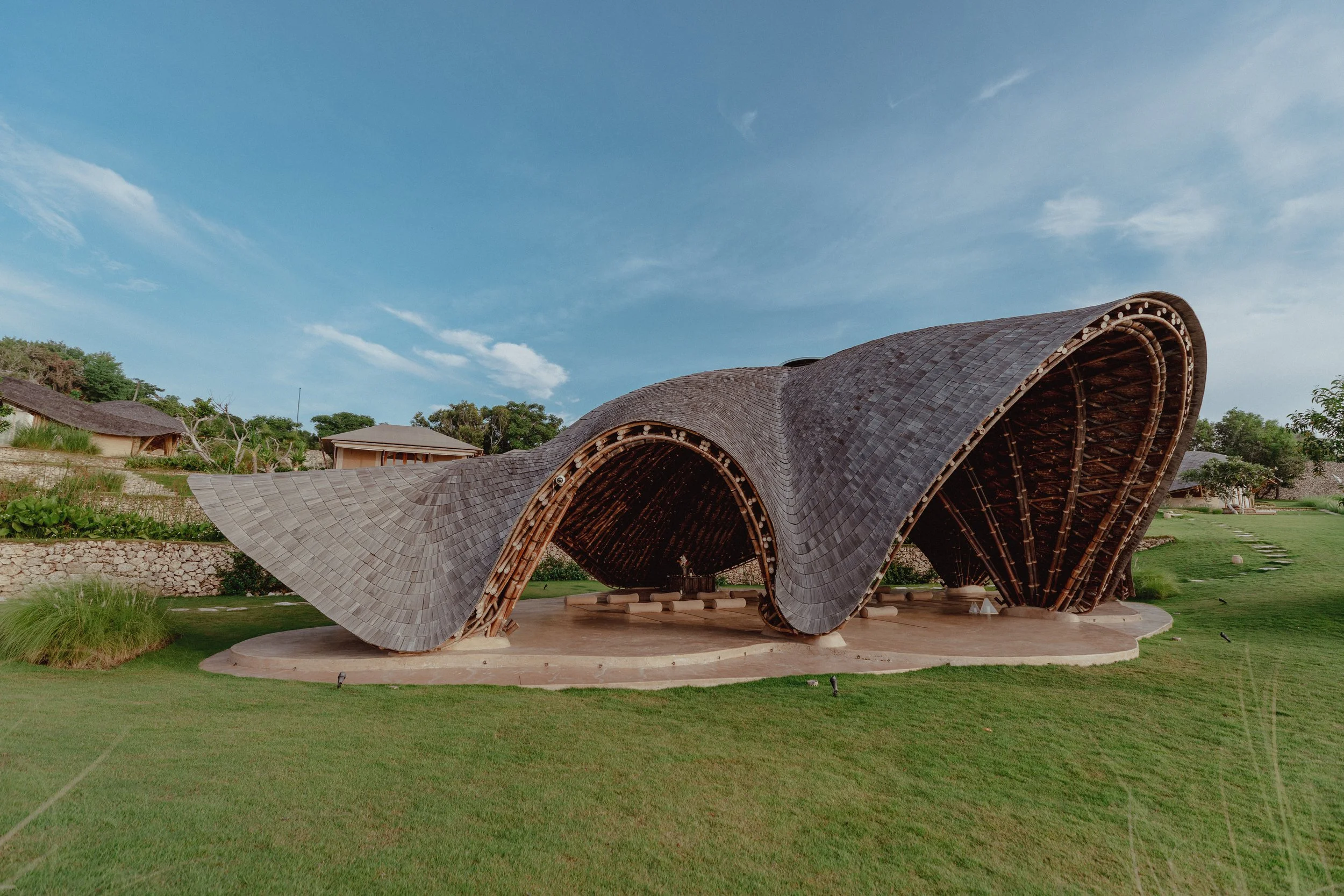Unique architectural building with curved wooden roof structure on a green lawn under a blue sky.