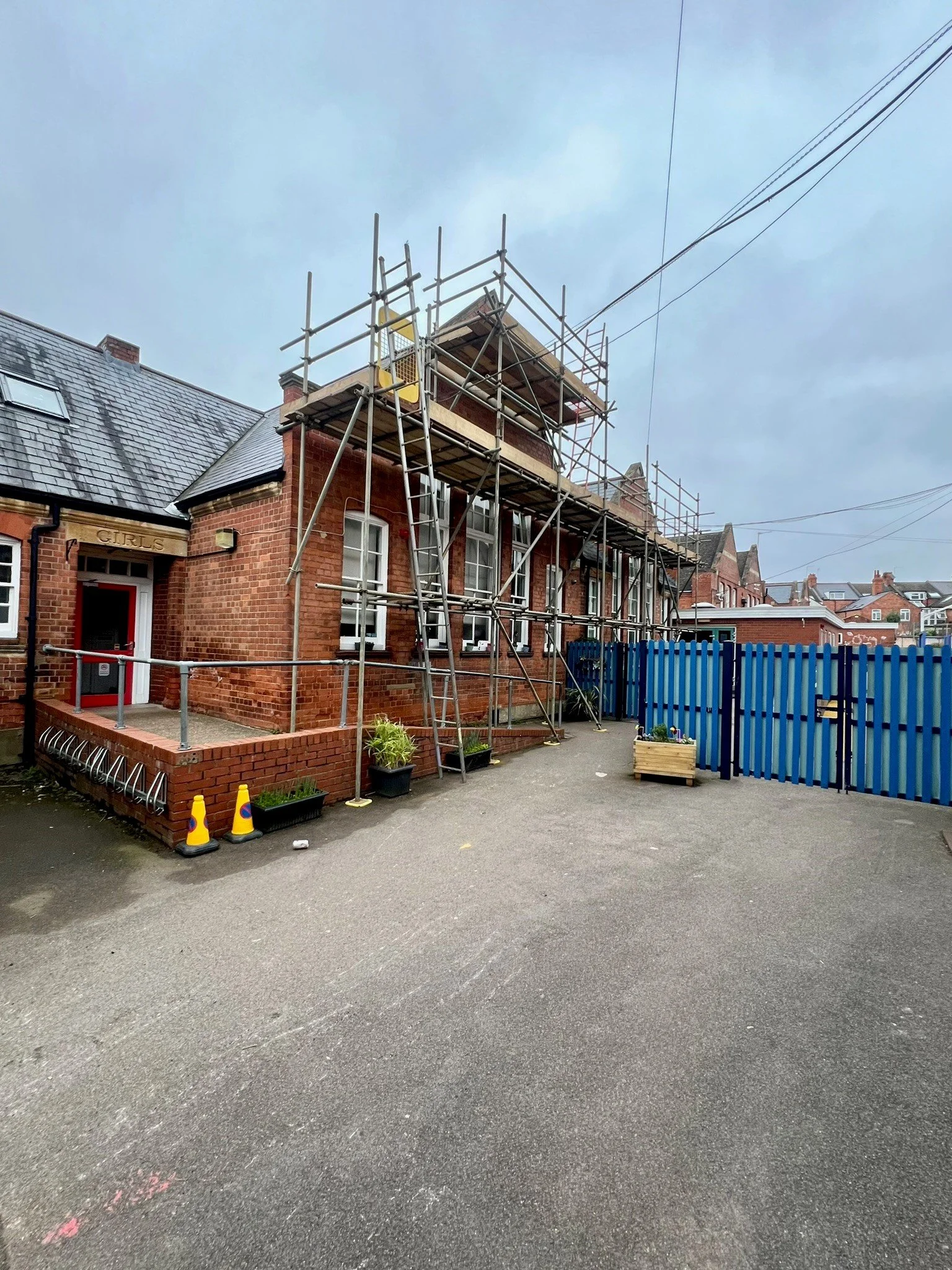 A brick school building undergoing emergency roofing repairs with scaffolding set up around it
