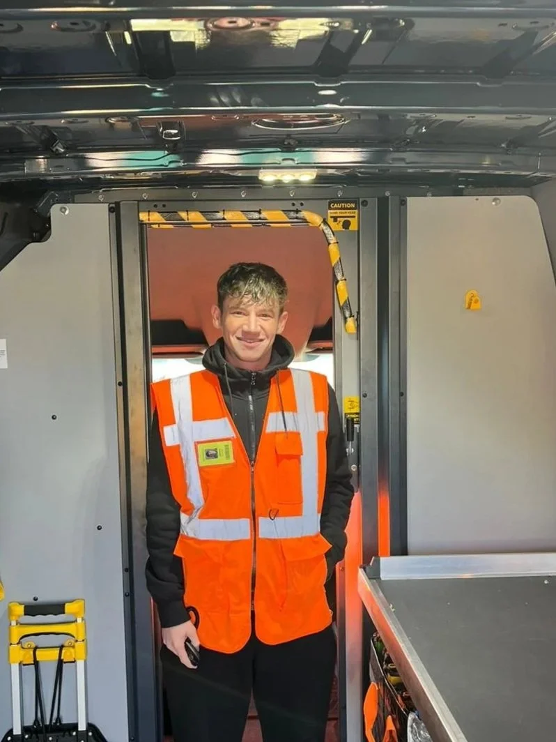 A delivery person loading a package from a blue Amazon Prime van in a residential neighborhood.