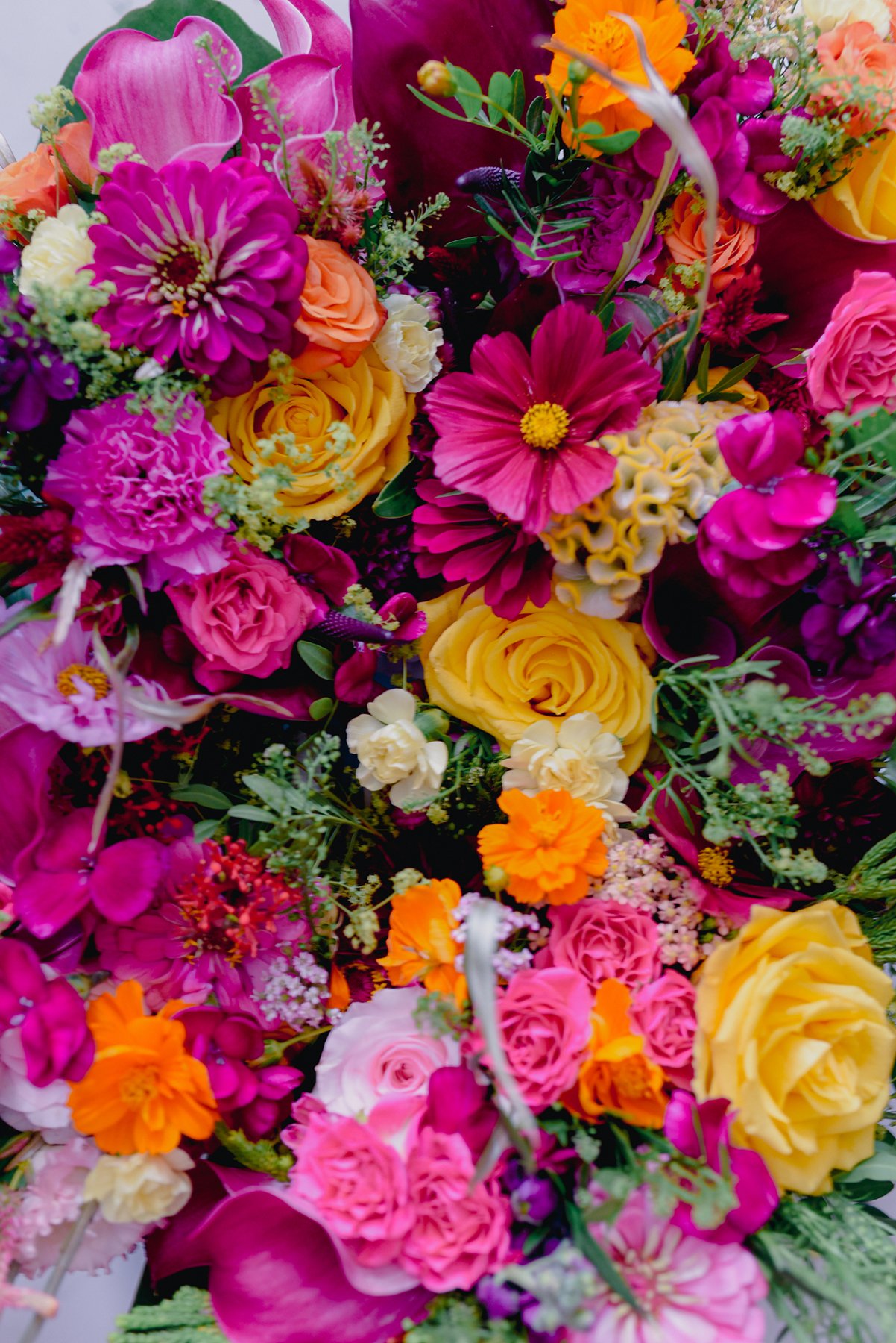 Un bouquet de fleurs colorées comprenant des roses, des tournesols, des zinnias, des oignons de fleurs, et des lys dans des tons de rose, violet, orange et jaune.