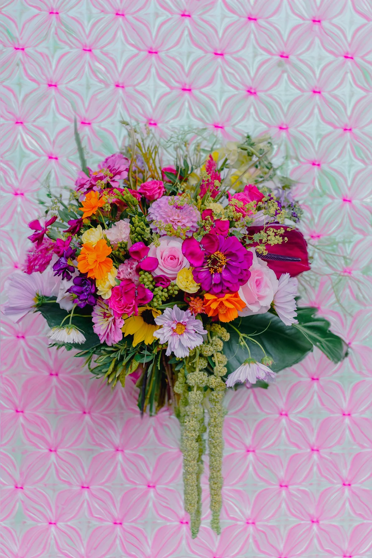 Un bouquet de fleurs colorées contre un fond rose et blanc avec un motif géométrique.