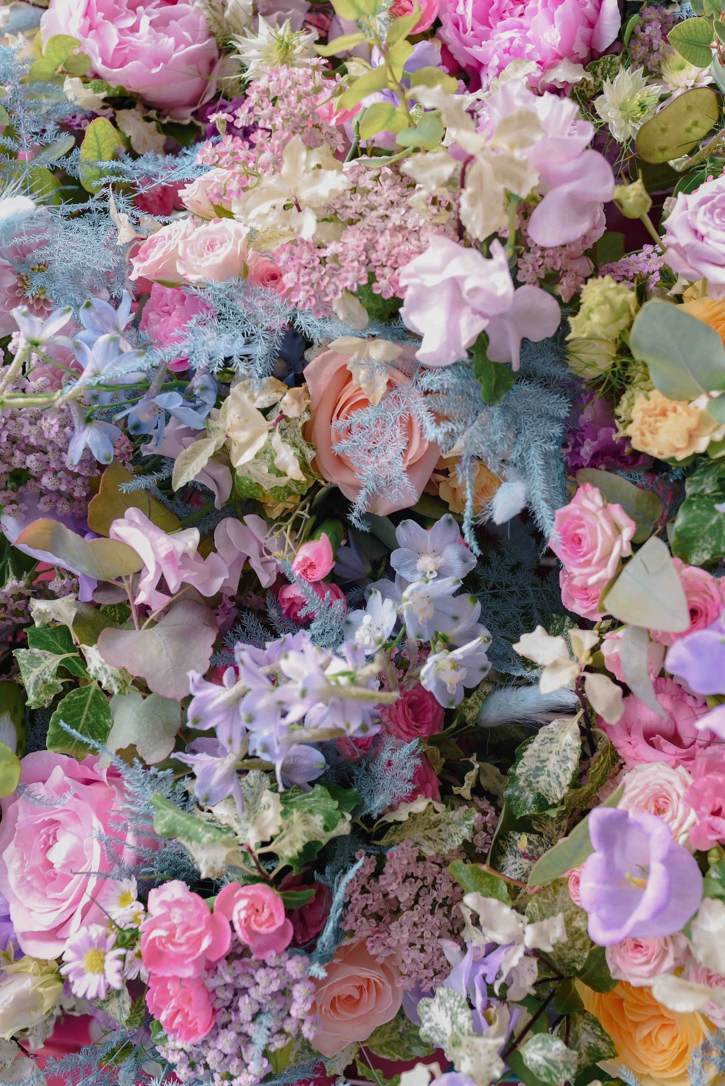 Un bouquet de fleurs colorées comprenant des roses, des lis, des hortensias et d'autres fleurs de différentes couleurs pastel, avec des feuillages.