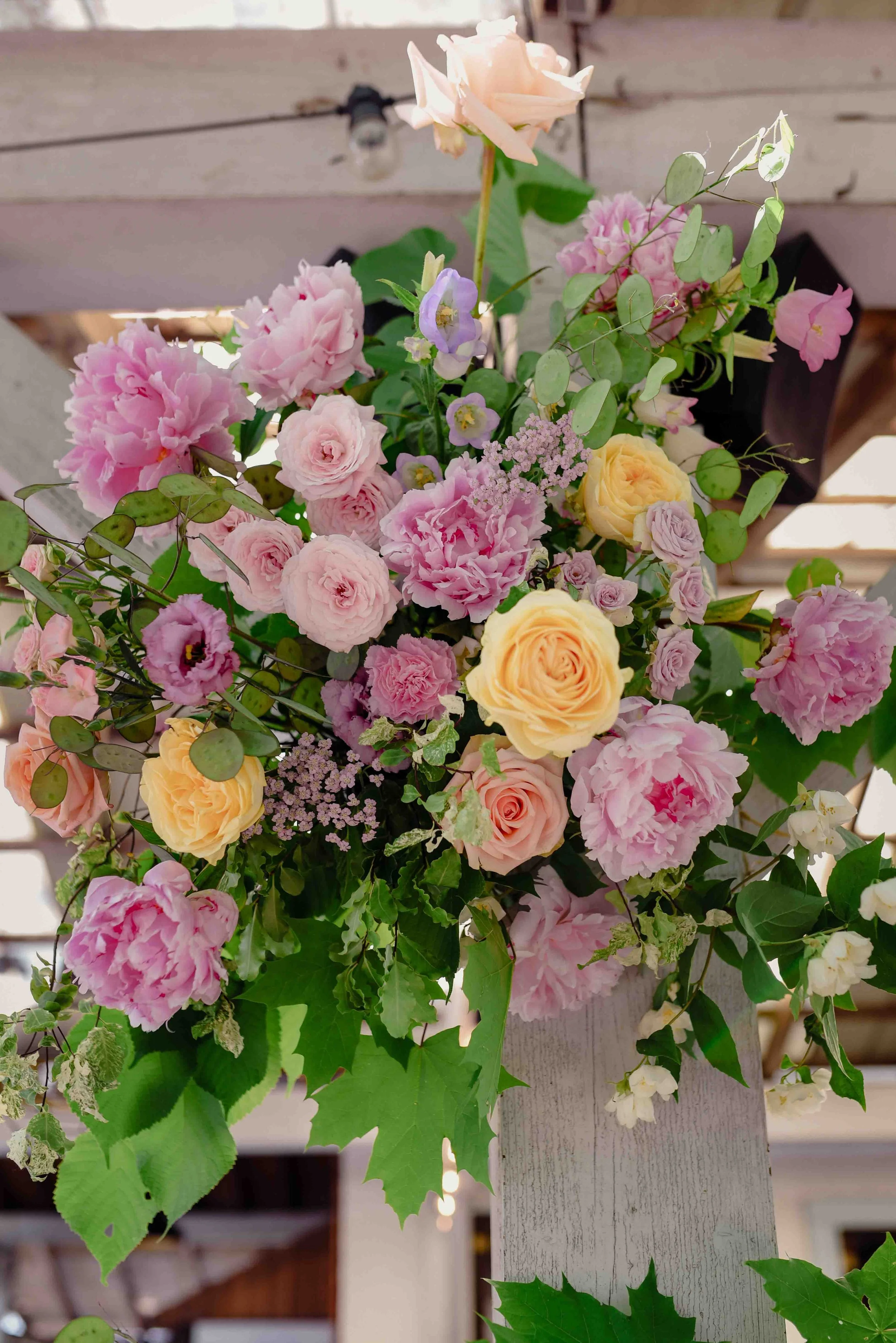 Un bouquet de fleurs composé de roses roses et jaunes, avec des feuilles vertes, fixé sur une structure en bois peint en blanc.