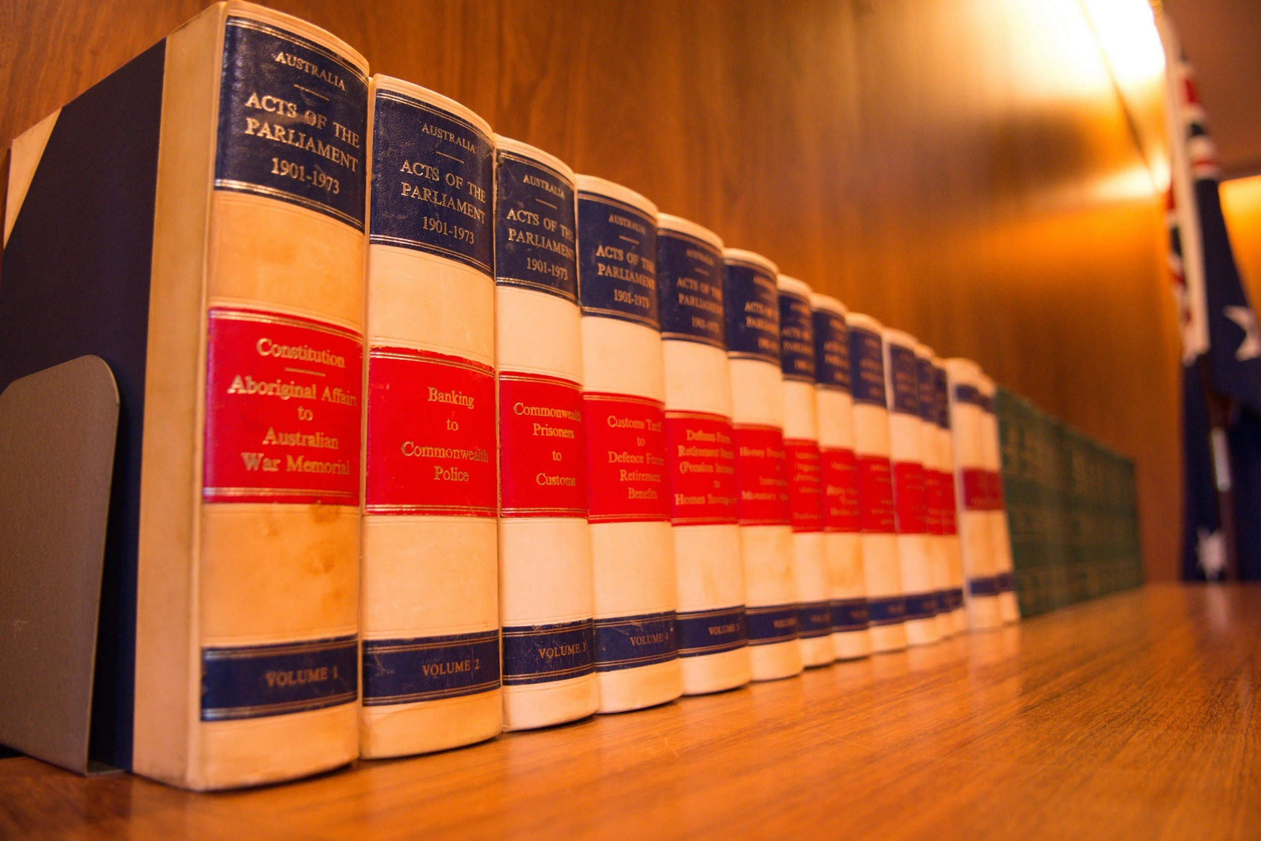 Series of hardcover books titled "Acts of the Parliament 1901-1973" and related topics, placed on a wooden shelf.