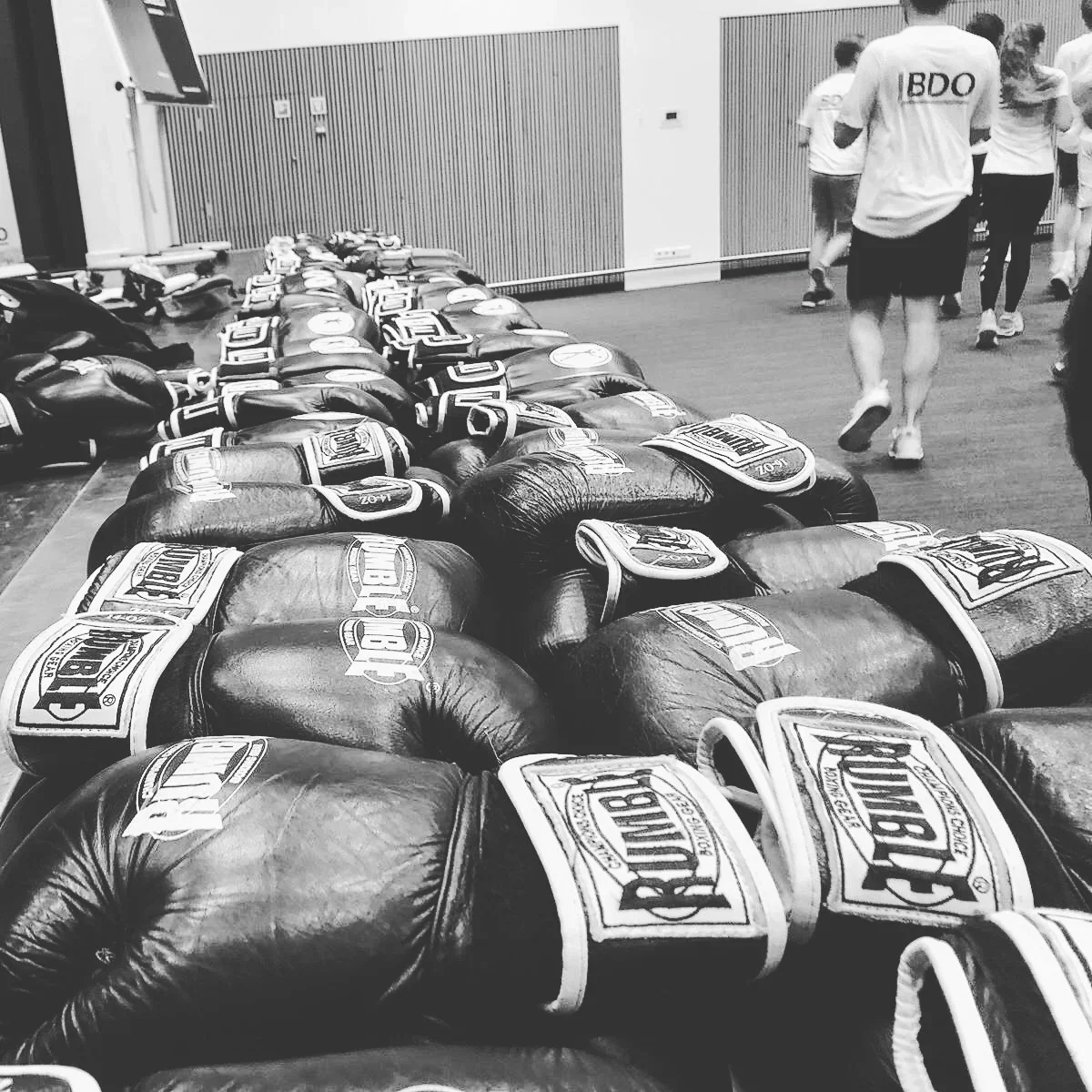 A line of boxing gloves with the CLETO REYES brand logo on them, set up on the floor in a training room. People are walking in the background.