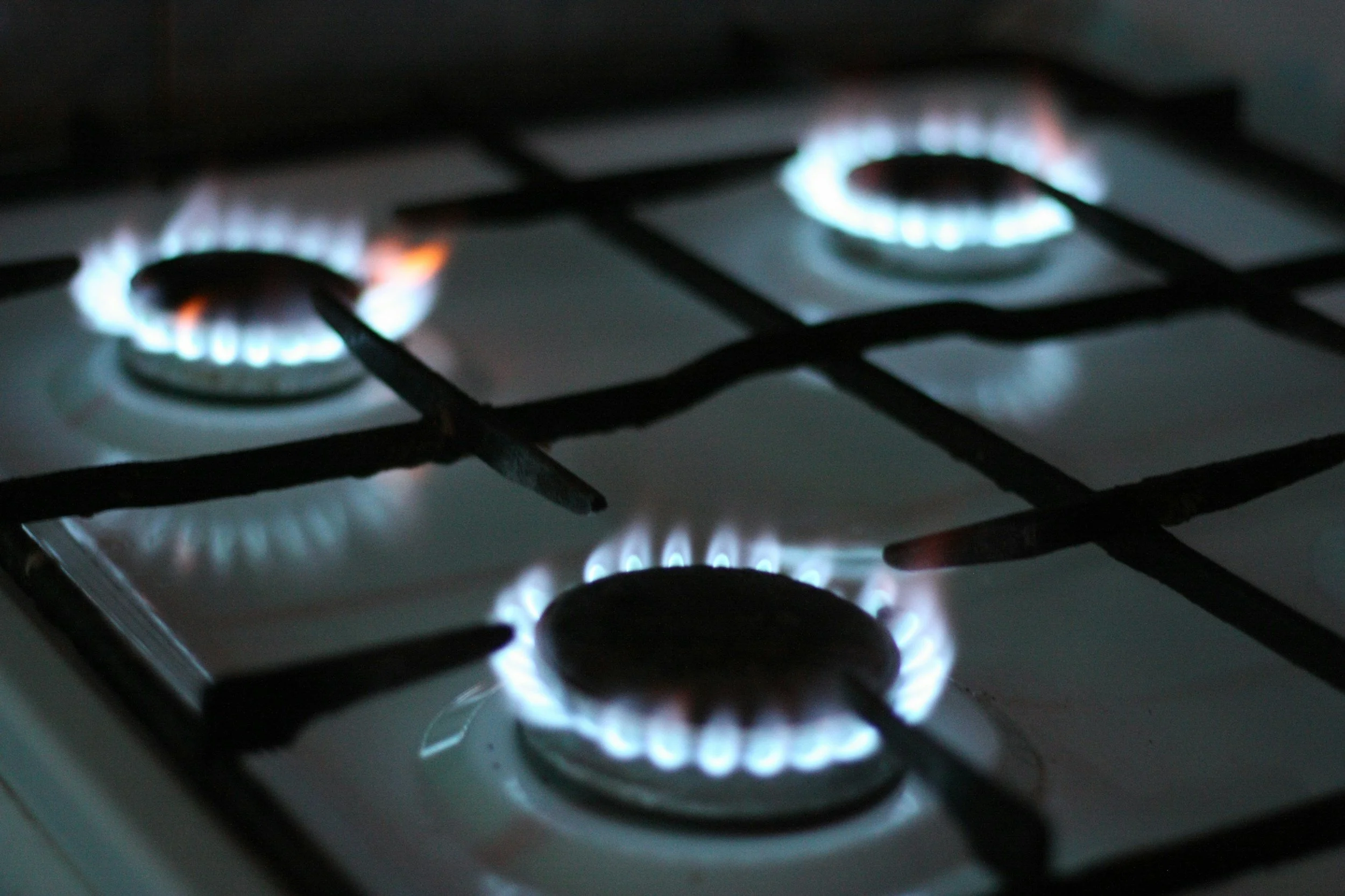 Three lit burners on a gas stove top are lit with a blue and orange flame. .