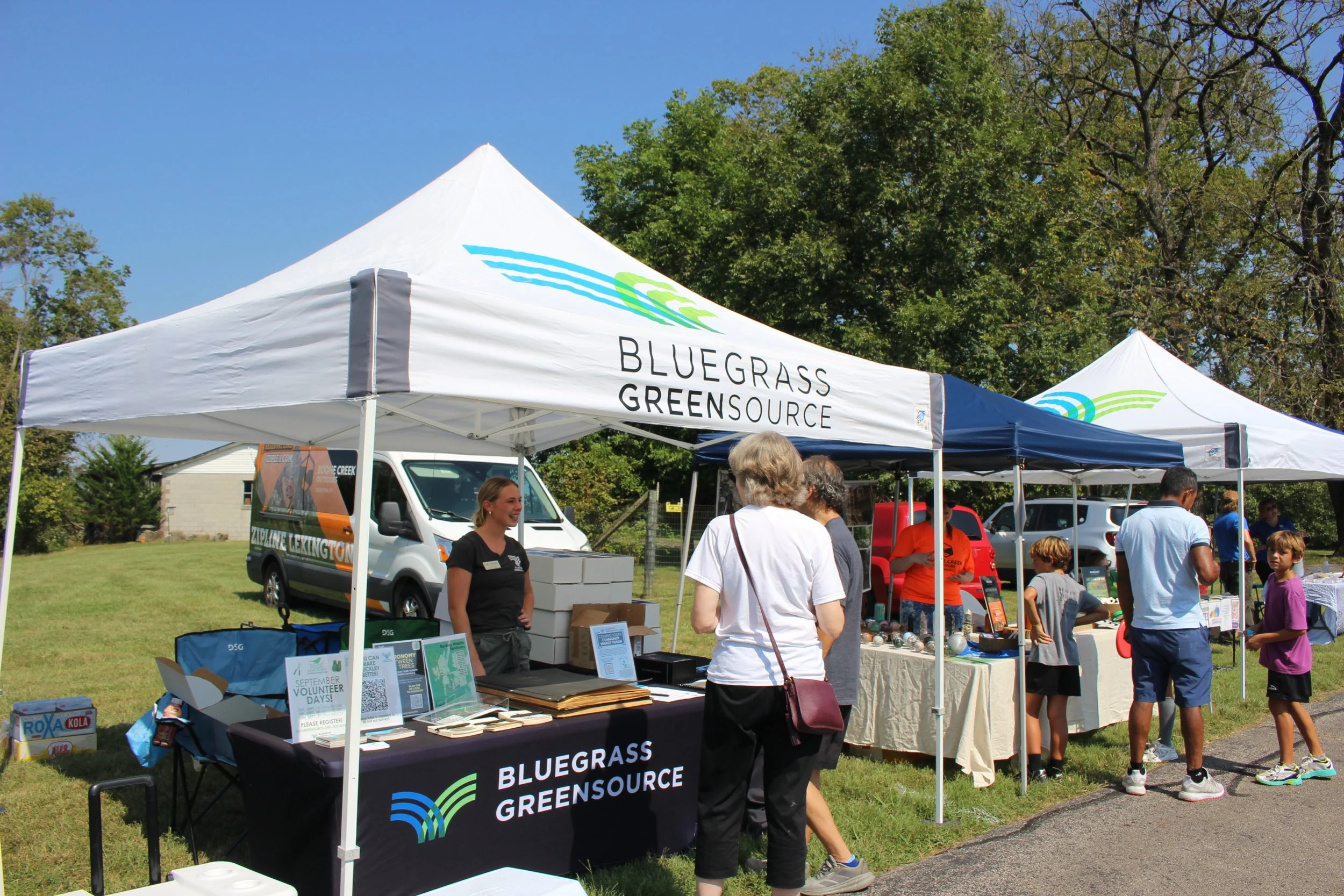 A couple speaks with staff at a white Bluegrass Greensource branded tent.