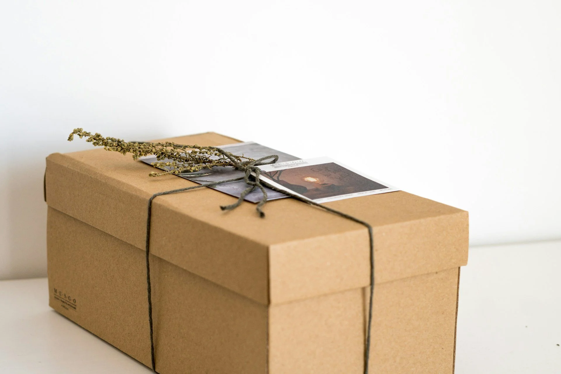 茶色の段ボール箱に、紐と乾燥した植物と写真が飾りとして付いている