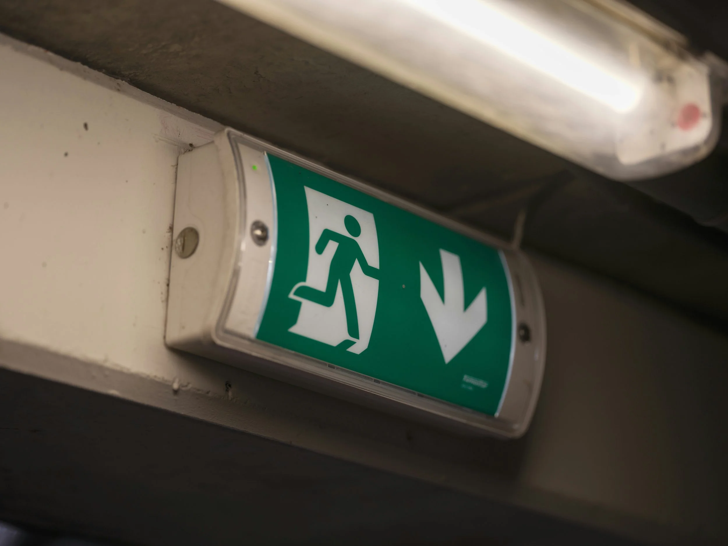 Emergency exit sign with a running figure and downward arrow.