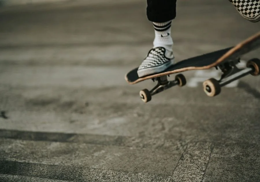 Enfant faisant un trick en skateboard, portant des chaussures à carreaux, des chaussettes rayées et des pantalons noirs, sur une surface de skate.