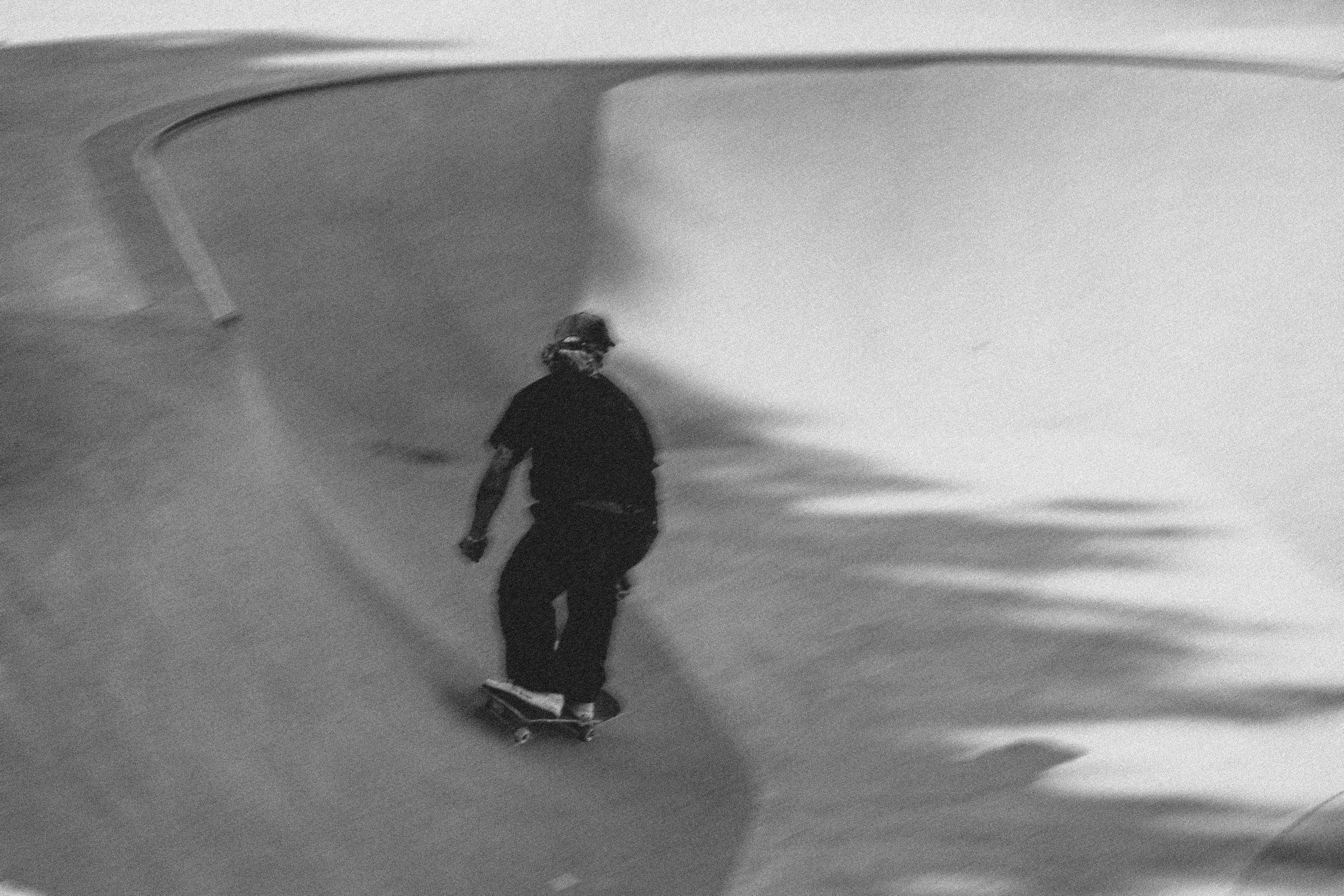 Un skateur dans un skatepark en noir et blanc, effectuant une descente dans une rampe en béton.