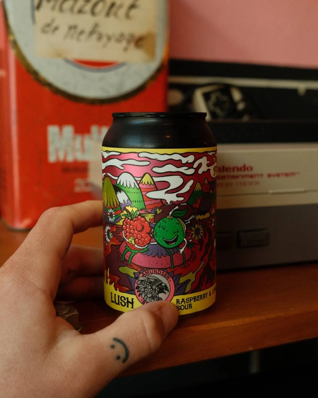 Une canette de boisson aromatisée à la framboise et à la baie de Lush, illustration colorée et joyeuse avec des fruits anthropomorphes, montagnes en arrière-plan, et un fond psychédélique.