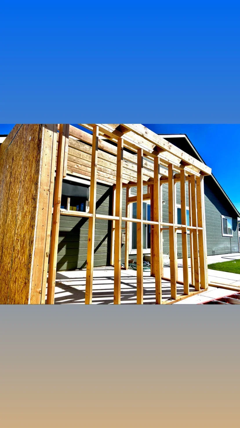 Wooden framing for an extension or porch being built on a house with green siding, under a clear blue sky.