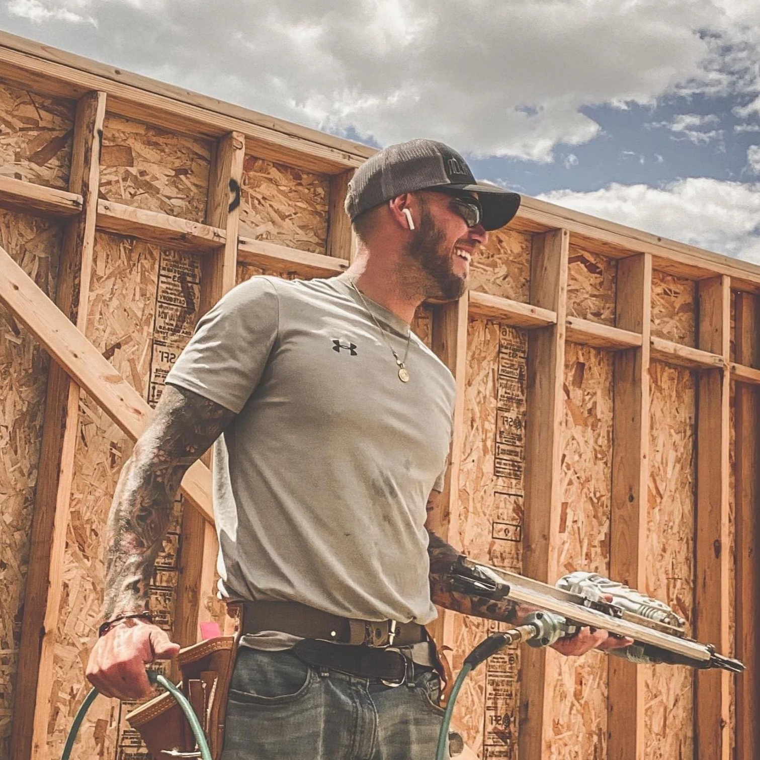 Troy Harris, owner of True Foundation Construction, at the construction site of a new custom built home with unfinished wooden framing, under a partly cloudy sky.
