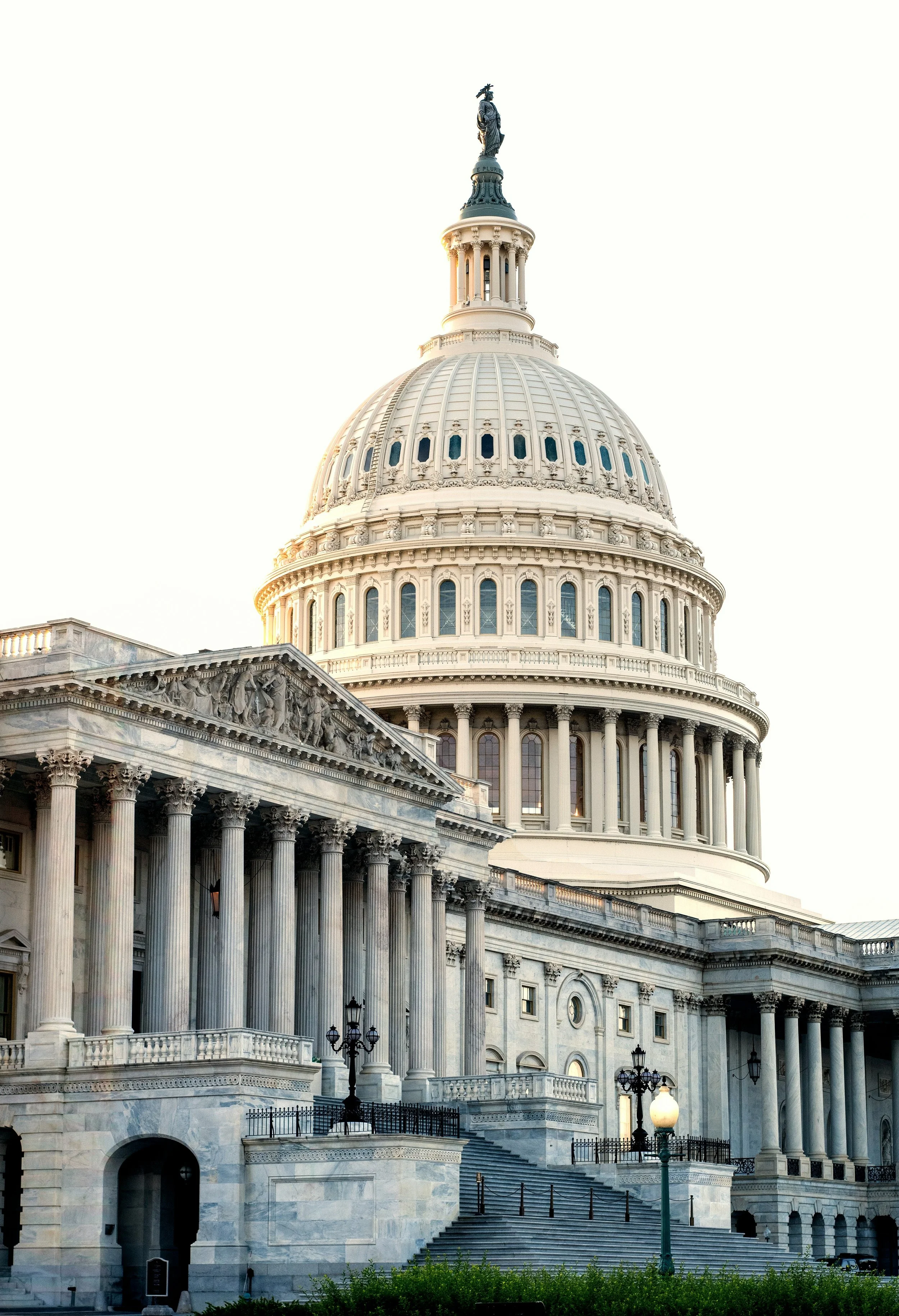 The United States Capitol building with its large dome and neoclassical architecture, featuring columns and steps, against a bright sky.