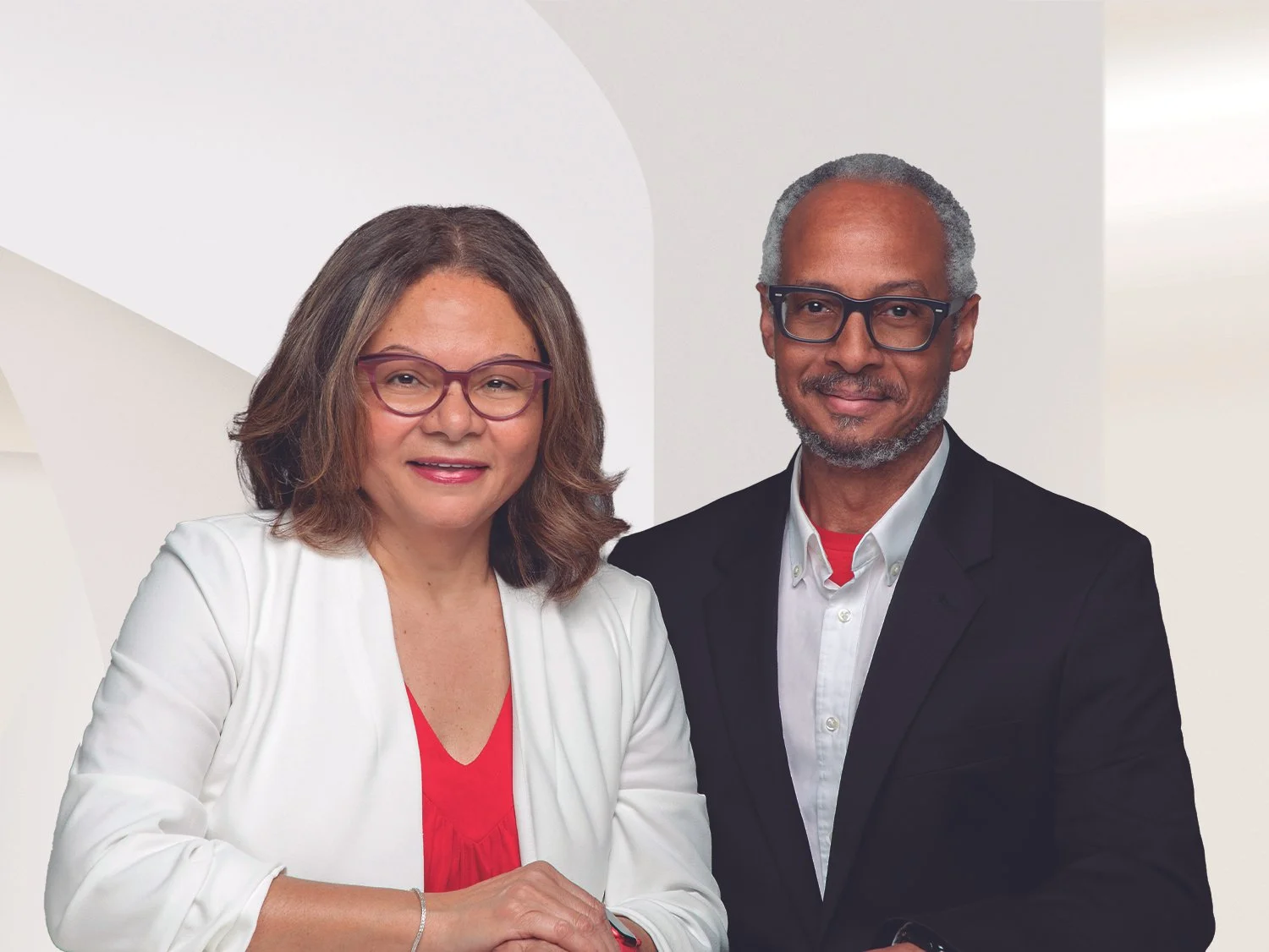 A woman and a man posing together indoors, both wearing glasses and professional attire, smiling at the camera.