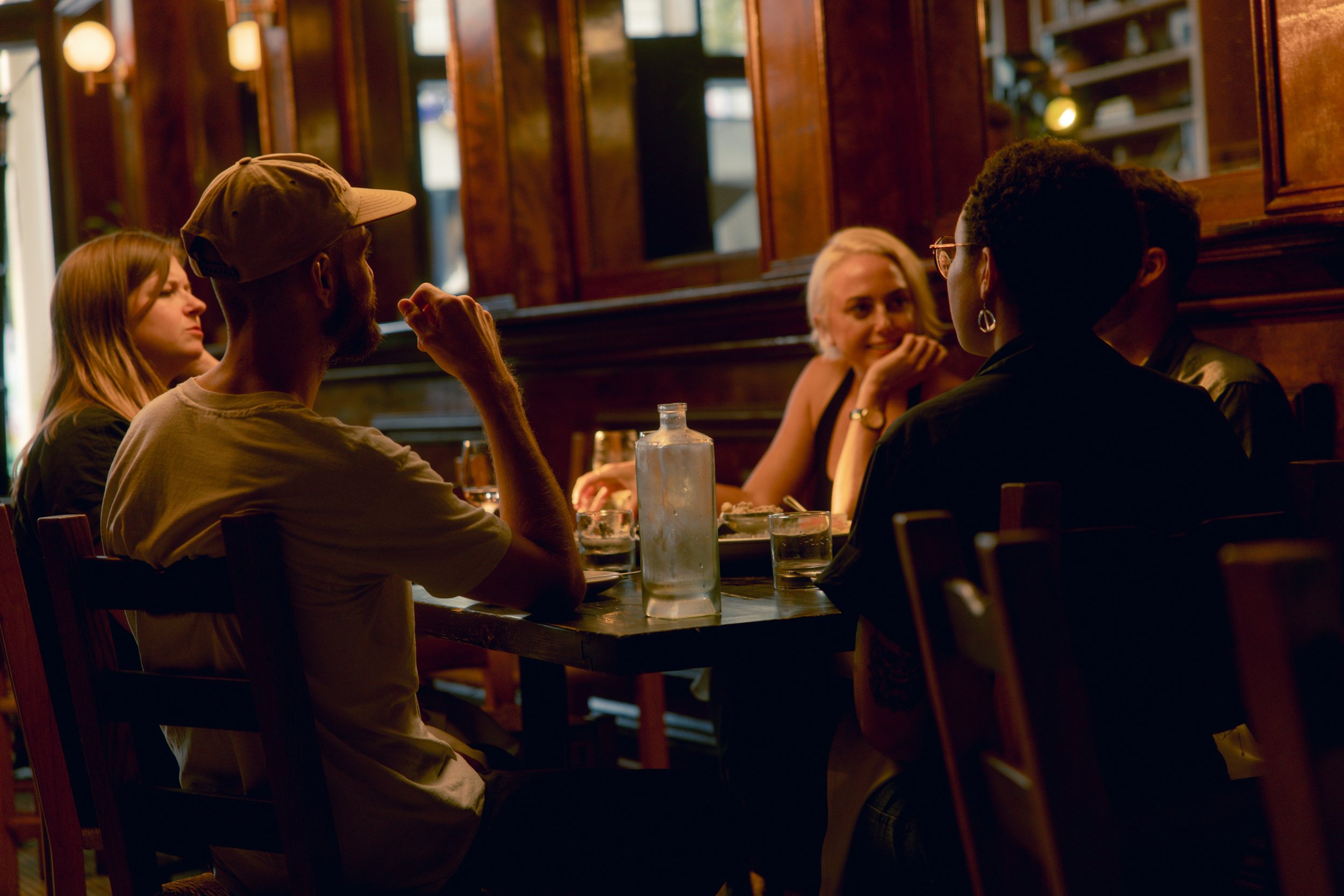 A group of five people sitting around a table in a dimly lit restaurant, engaged in conversation and enjoying their meal and drinks.