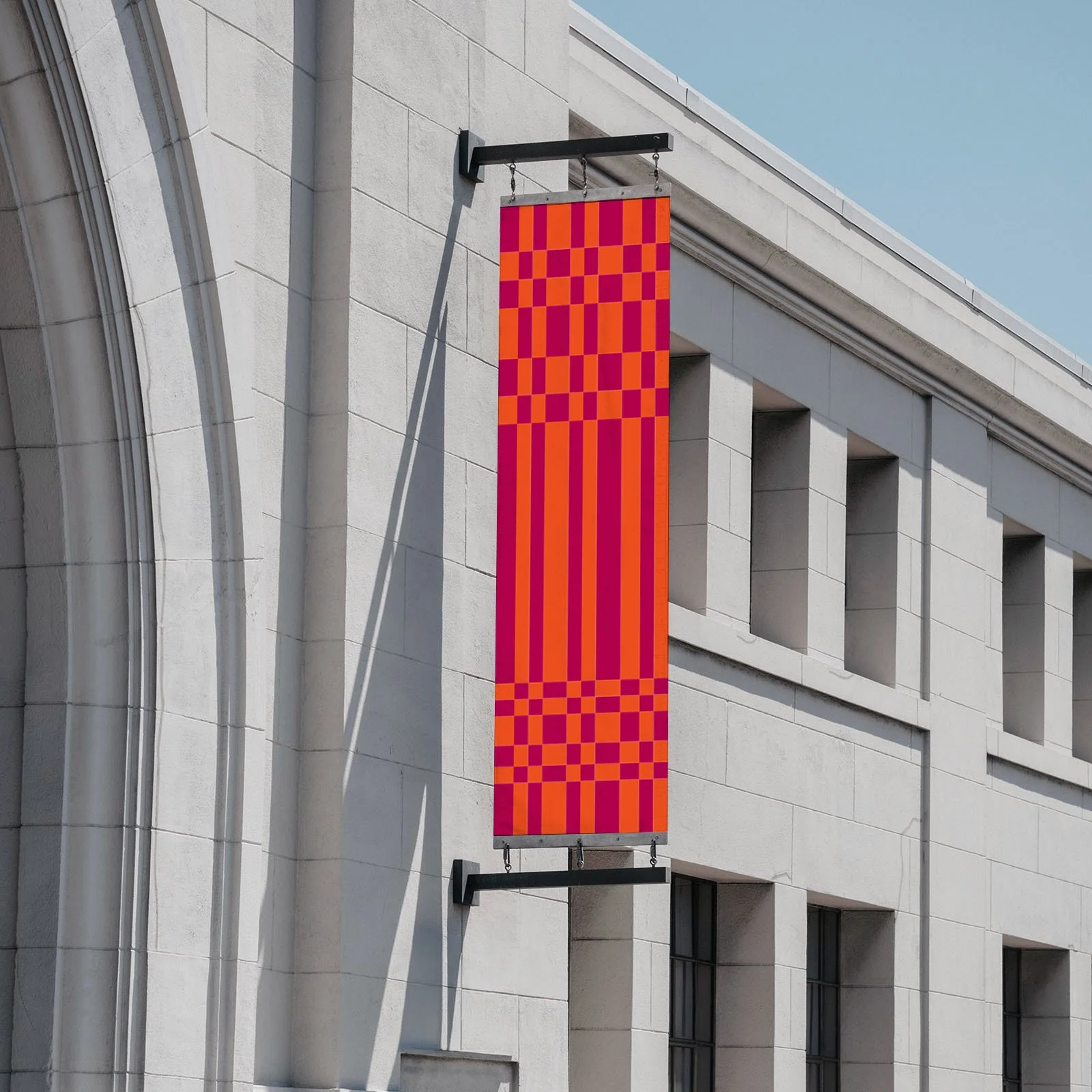 A vertical banner with red and purple squares and lines hangs on the side of a white stone building under a blue sky.