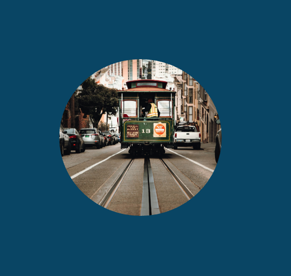 Vintage streetcar riding down a city street with parked cars and buildings in the background.