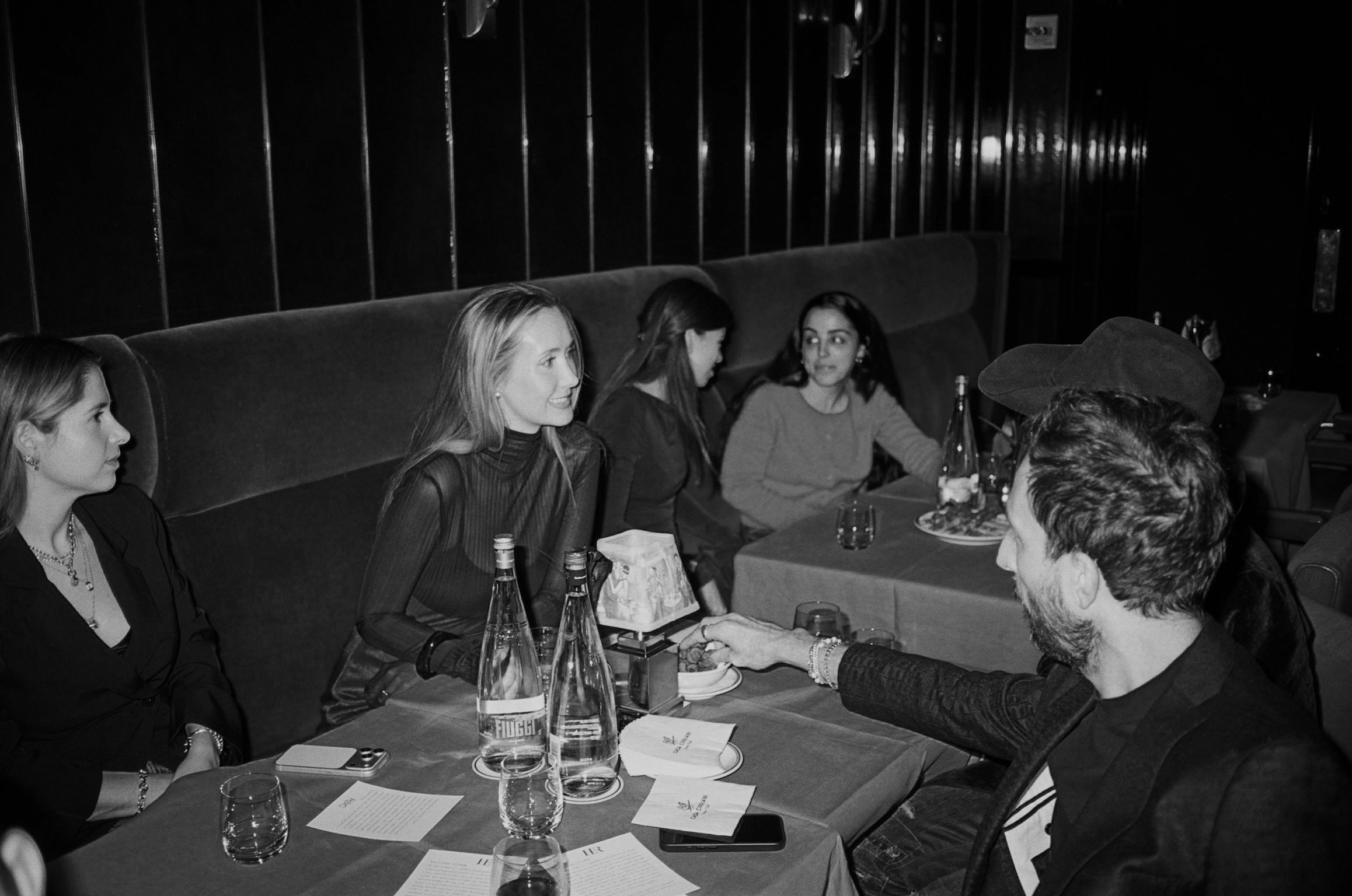 Group of people sitting at a table in a restaurant or bar, with drinks and menus on the table, engaged in conversation.