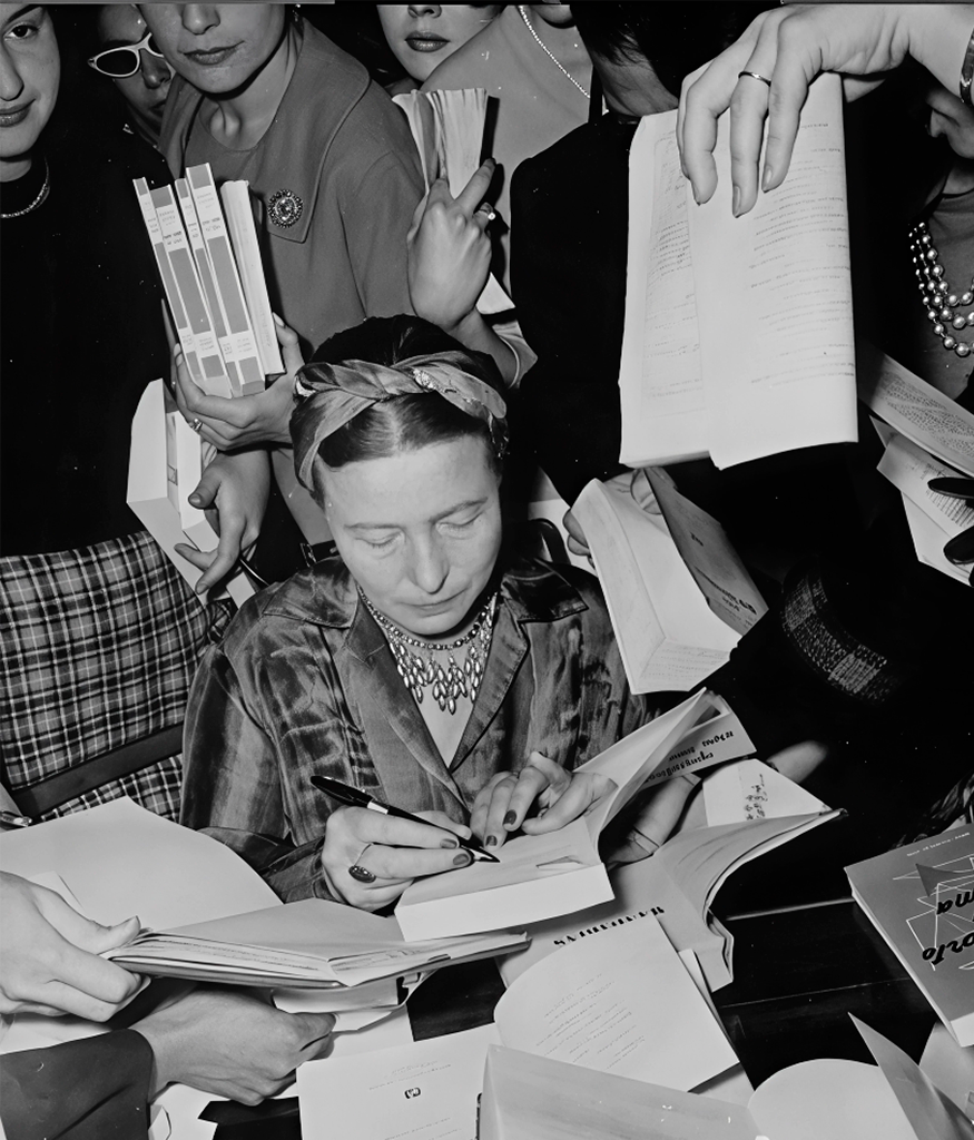 A woman is signing a book surrounded by multiple people holding books and documents.