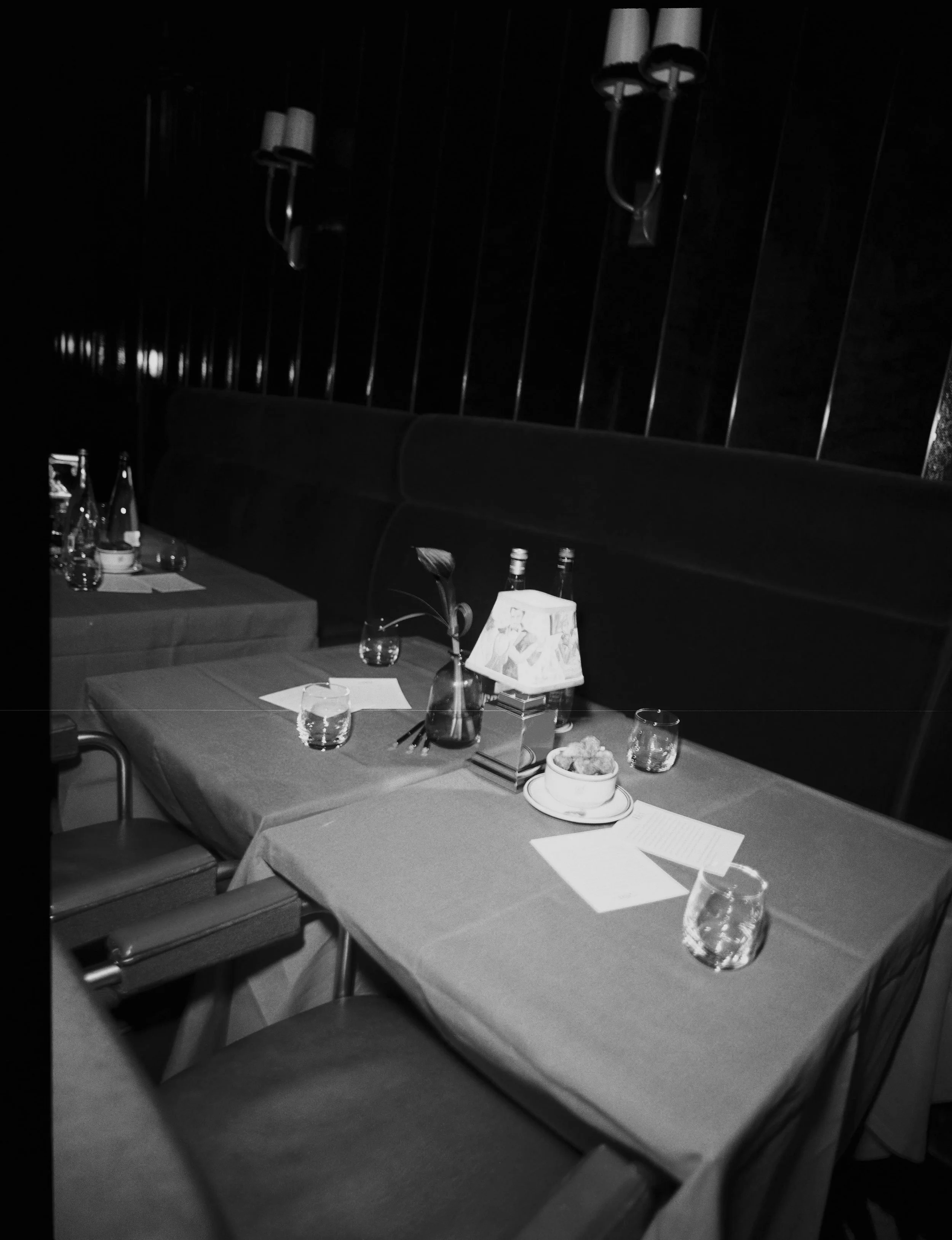 Empty restaurant table set with glasses, a lamp, and a flower vase in a dimly lit room.
