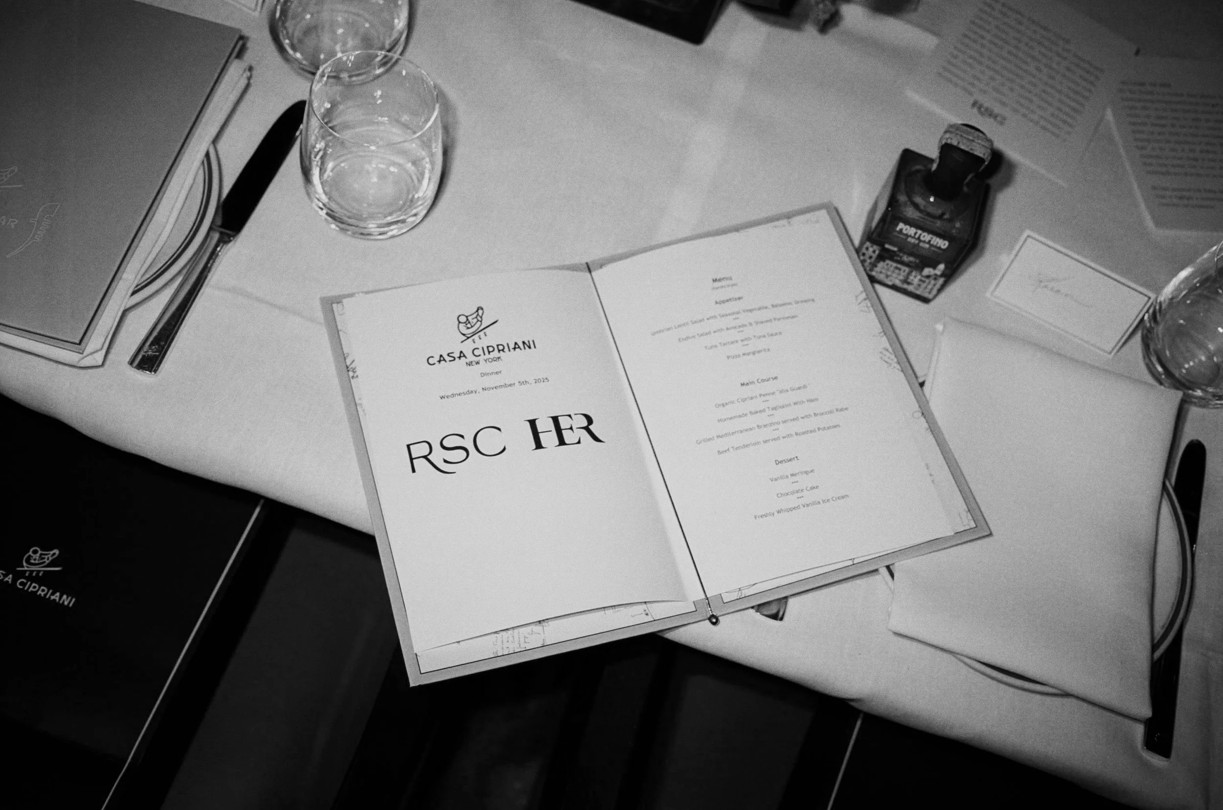 Black and white photo of a restaurant table setup with glasses, menus, a knife, and a bottle of Portofino liquor.