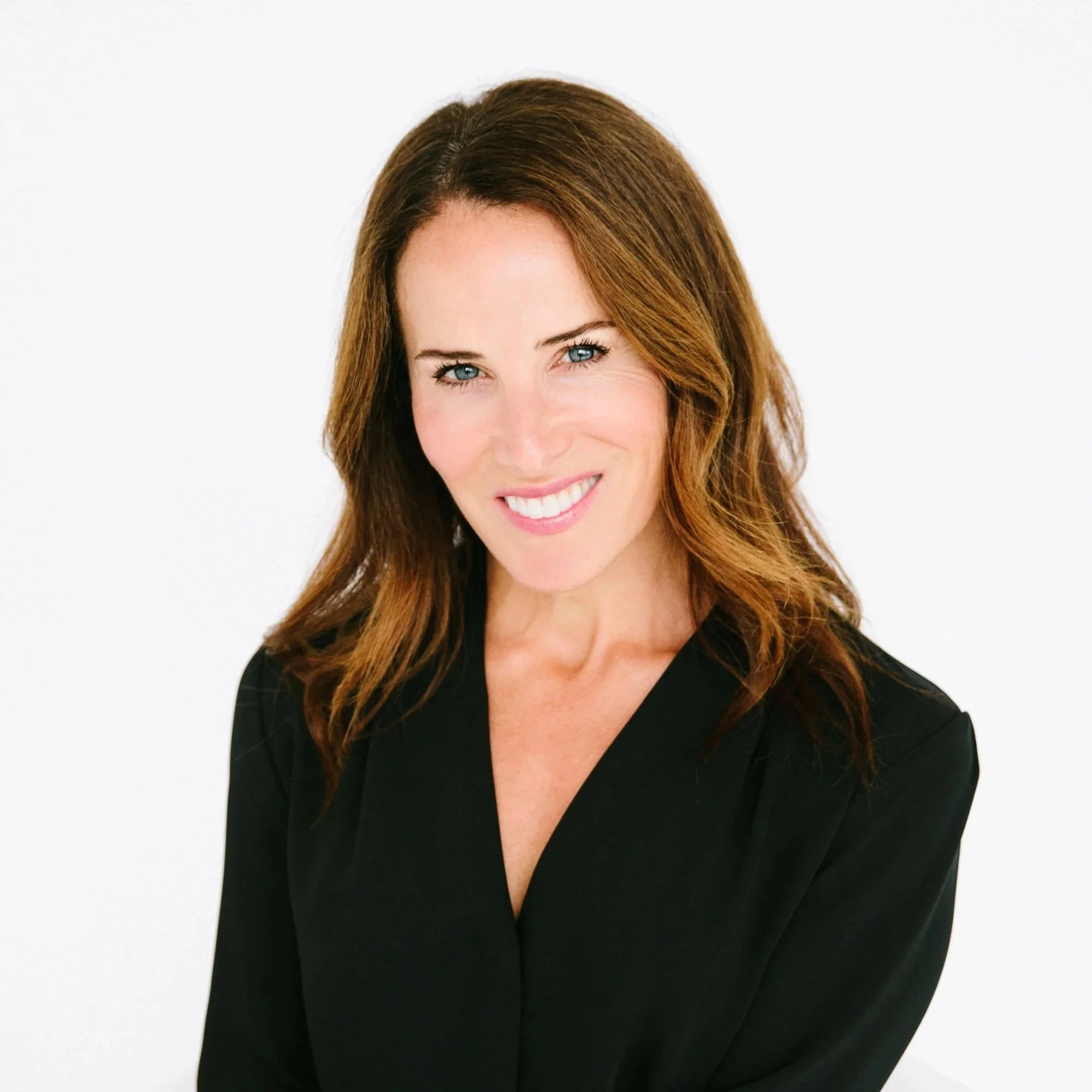 Dr. Sarah de la Torre, a woman with long brown hair, blue eyes, and a bright smile, wearing a black top against a plain white background.