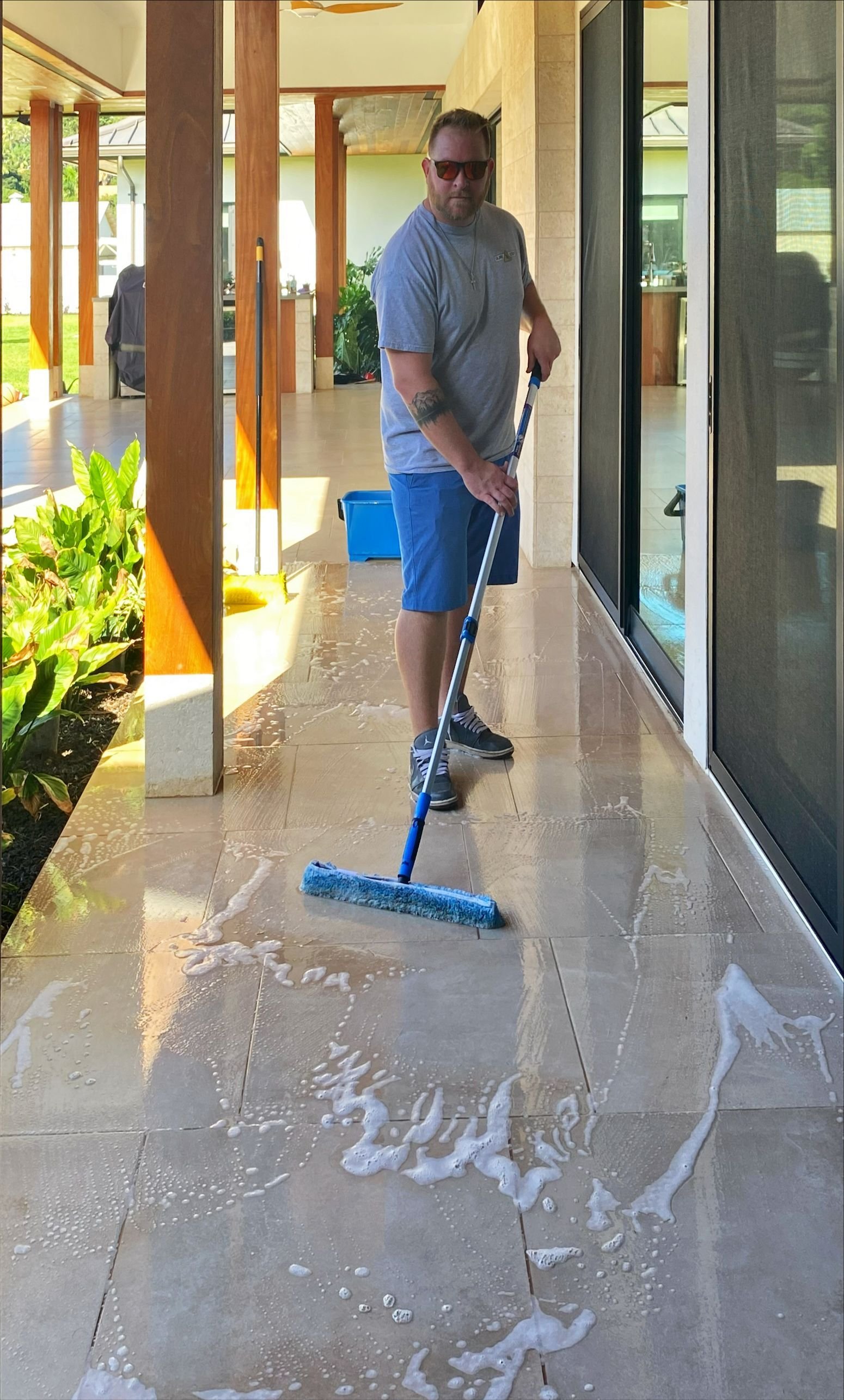 Man mopping wet tiles on a porch or patio area outside a house.