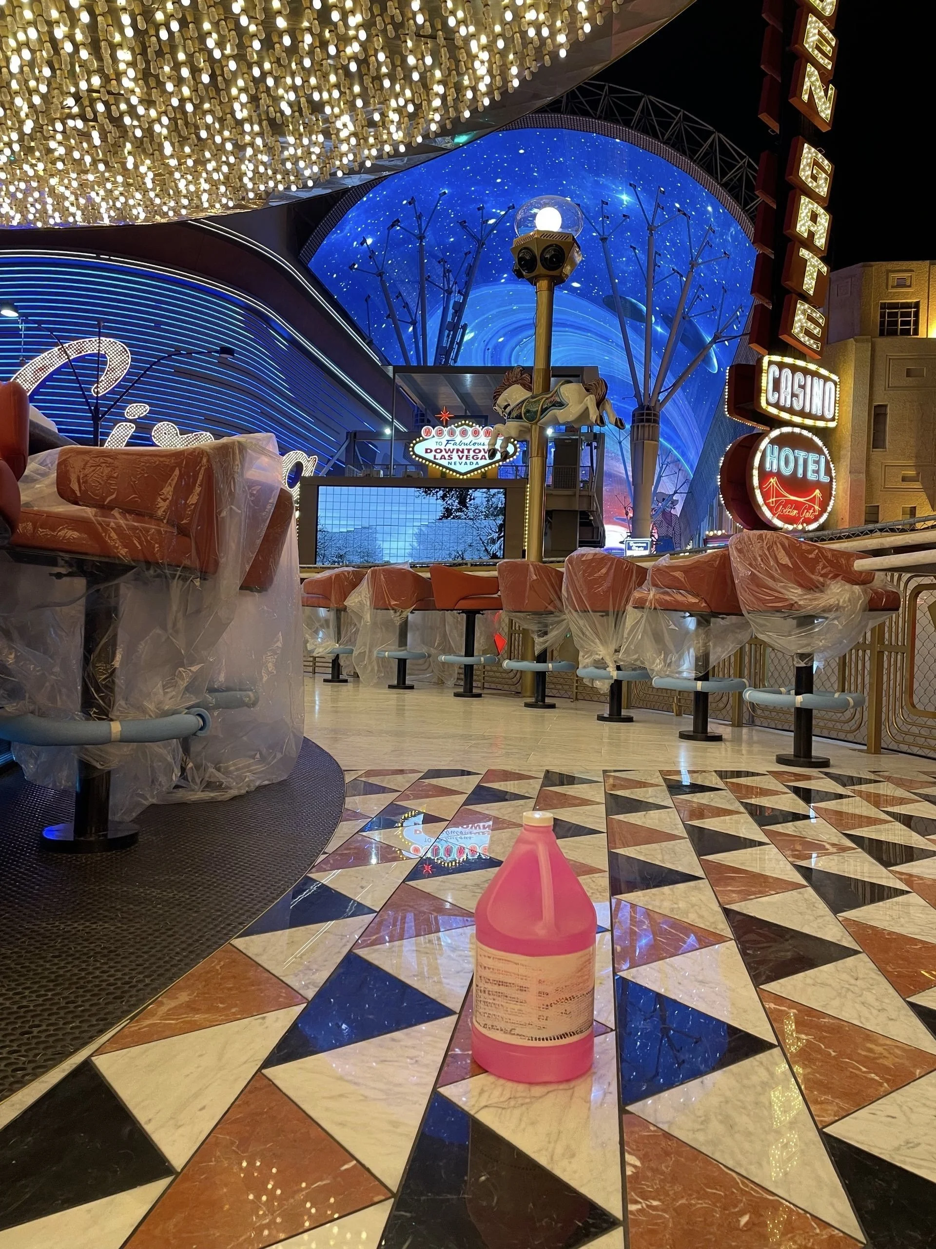 Indoor scene at a casino with colorful lights, a carousel horse, and a pink bottle of cleaning solution on a patterned tile floor after slip patrol non slip treatment. 