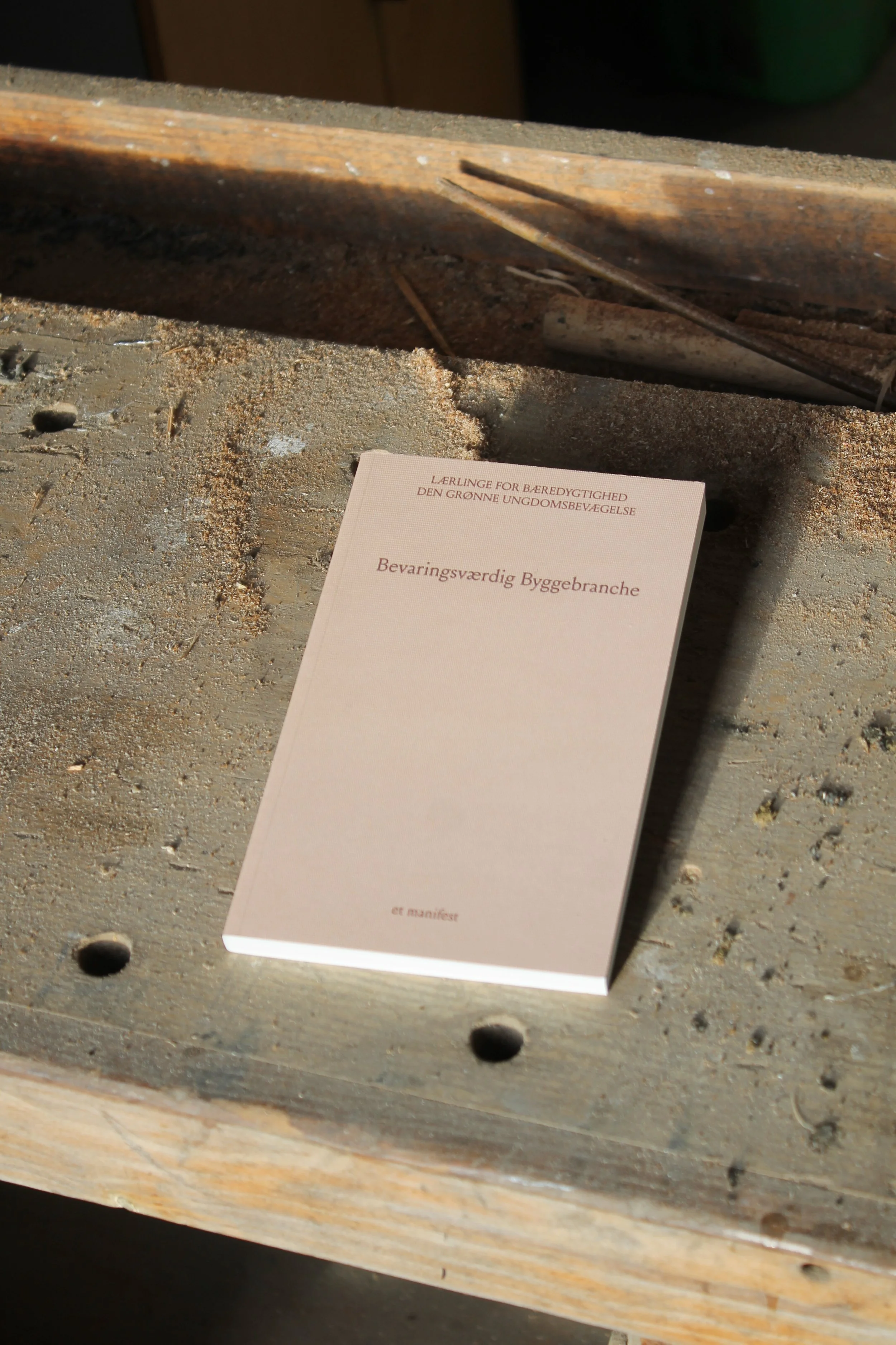 A pink book titled 'Bevaringsværdig Byggebranche' placed on a dusty workbench.