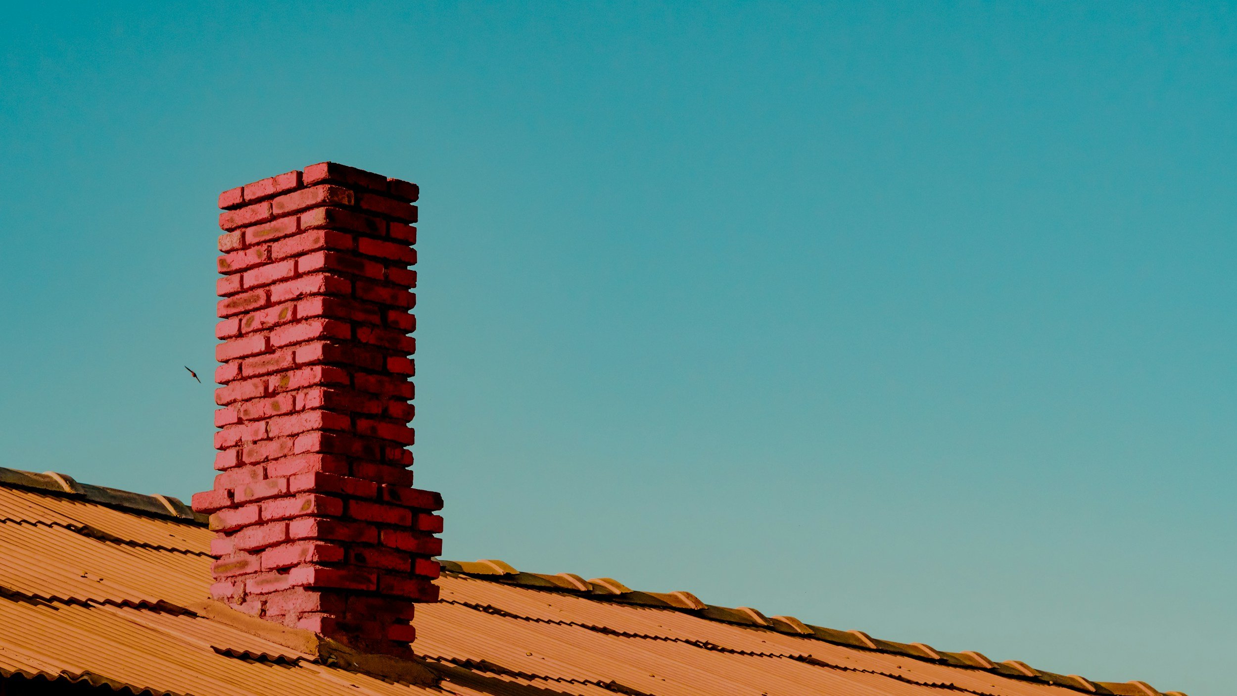 Red brick chimney on a tiled roof against a clear blue sky.