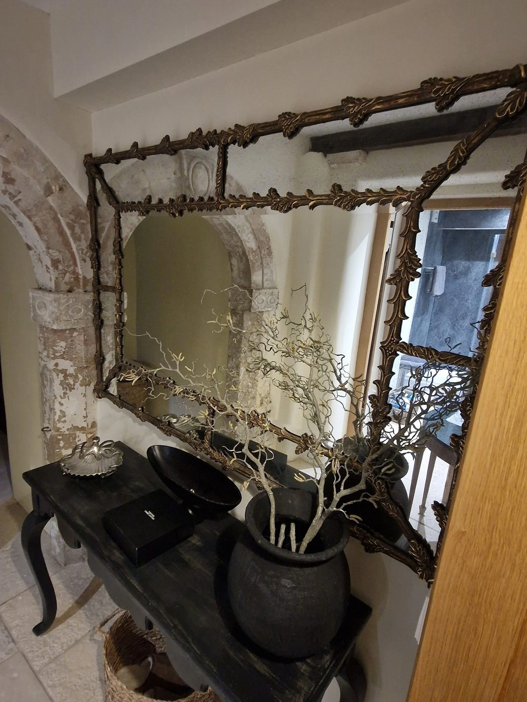 Decorative hallway with mirror, black table, potted plant, and vintage stone archway.