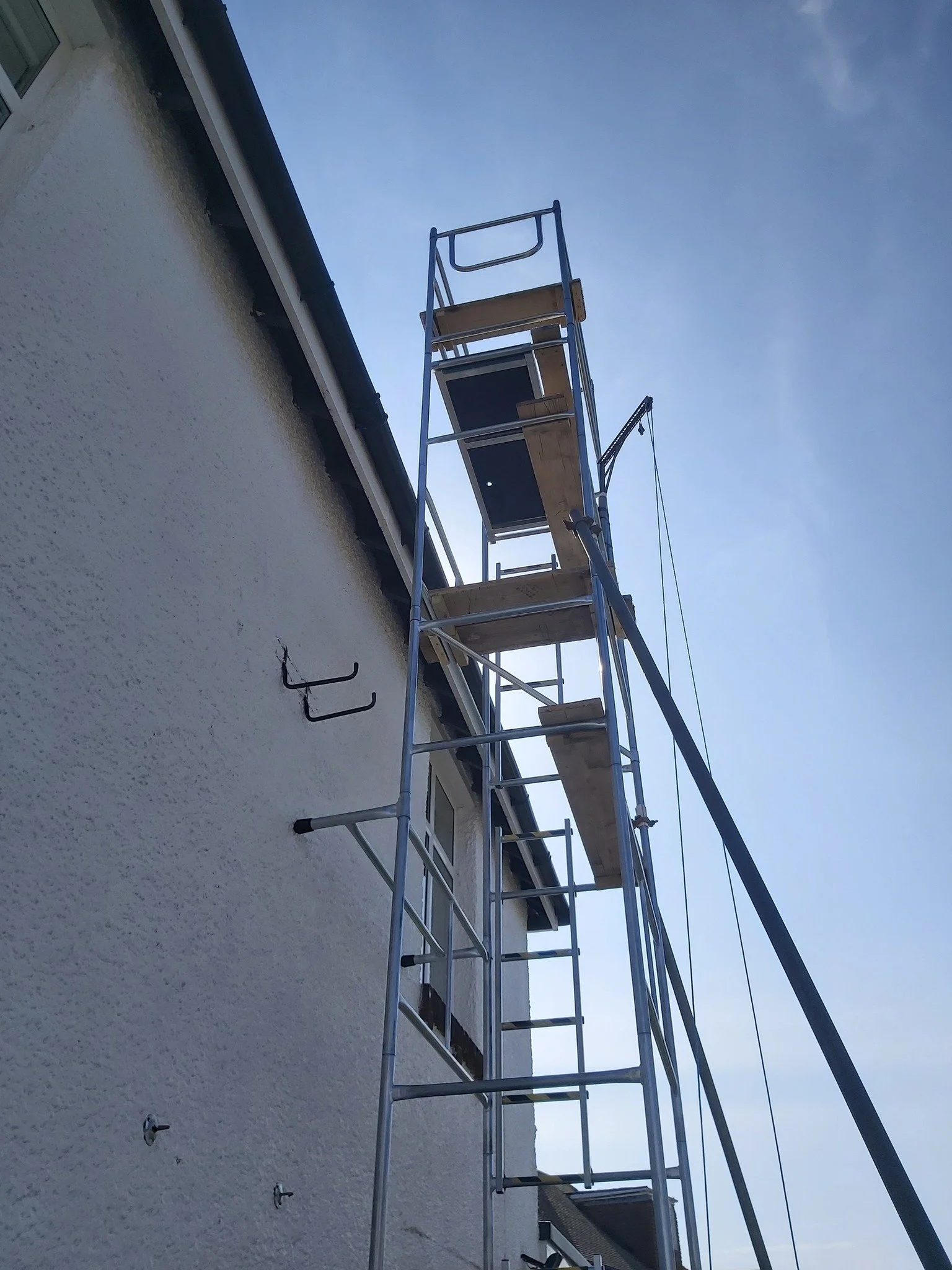 Construction scaffolding set up against the side of a building with a ladder leaning against it, and a clear blue sky in the background.