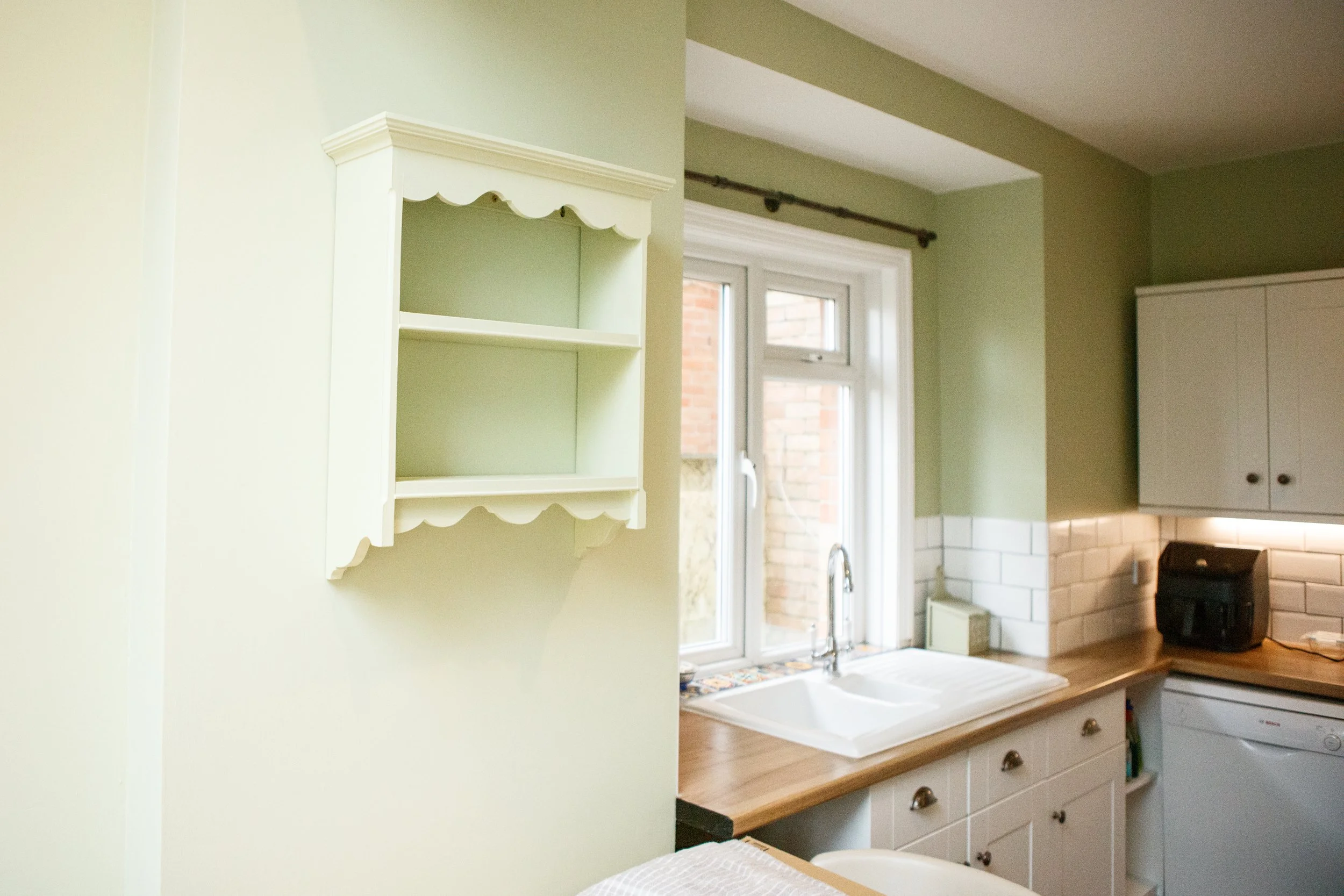 A kitchen with green walls, white cabinetry, a window over the sink, and a tiled backsplash.