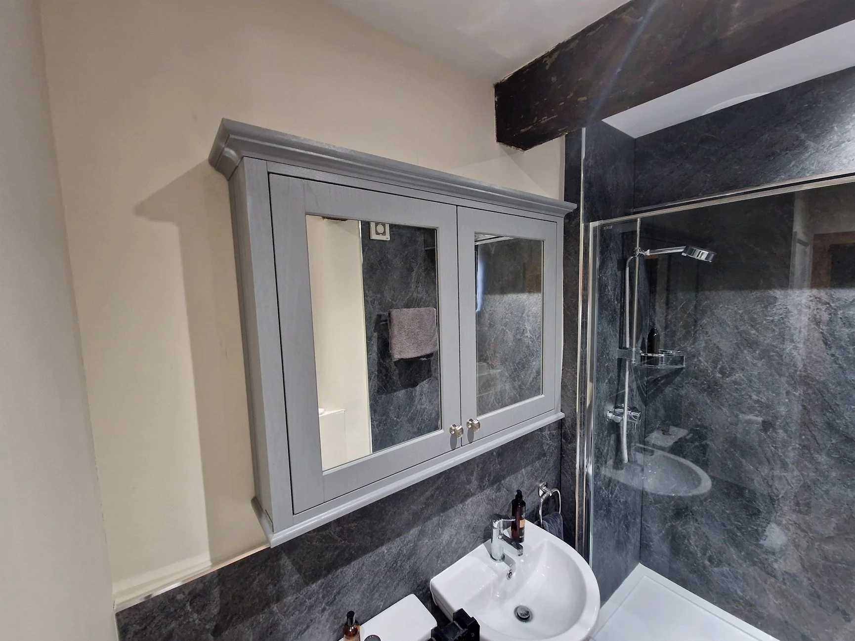 Bathroom with a shower, dark gray marble wall, white sink, gray wall cabinet with mirror, and beige wall
