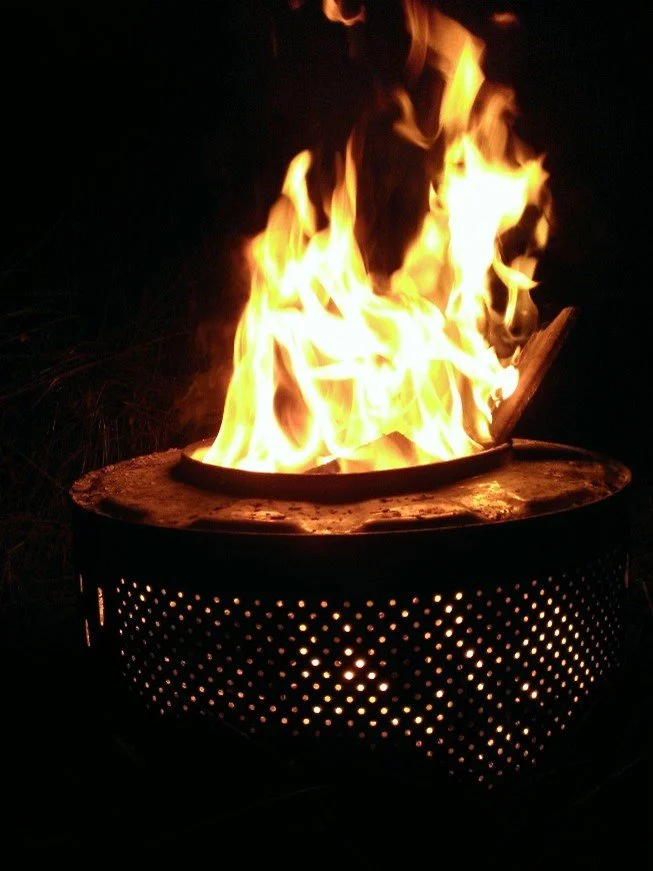 A fire burning in a metal fire pit at night with visible flames and glowing embers.