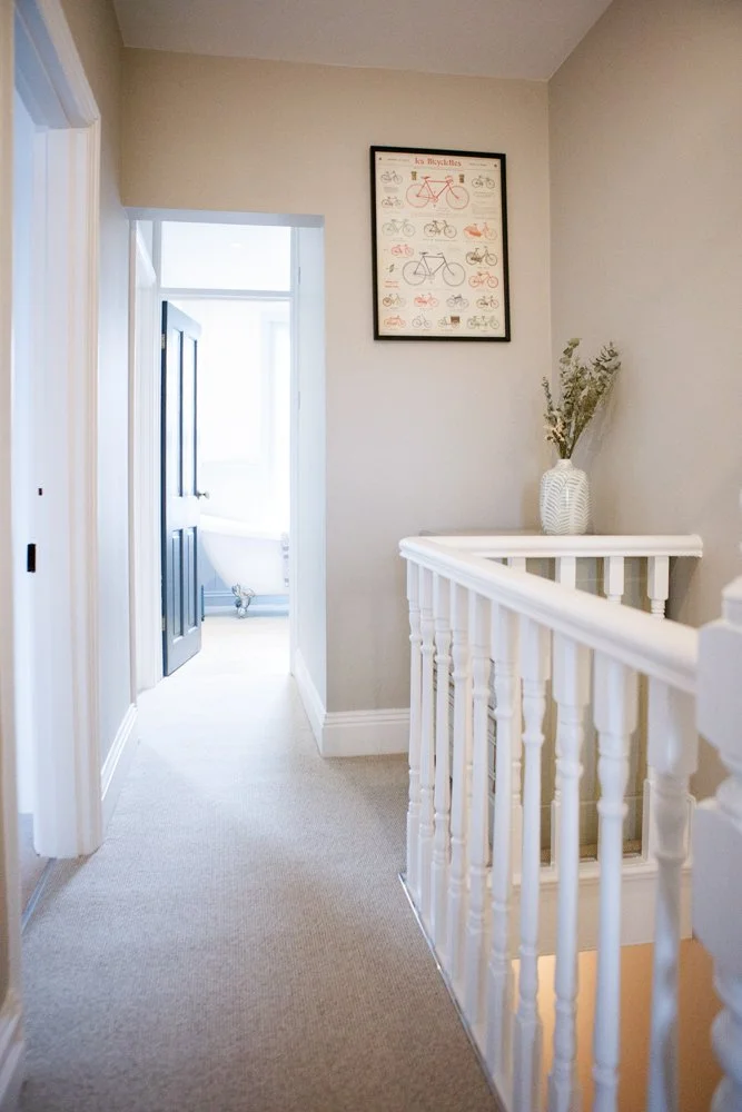 Hallway with a staircase and a framed poster of bicycles on the wall, with a vase and plants on the landing.