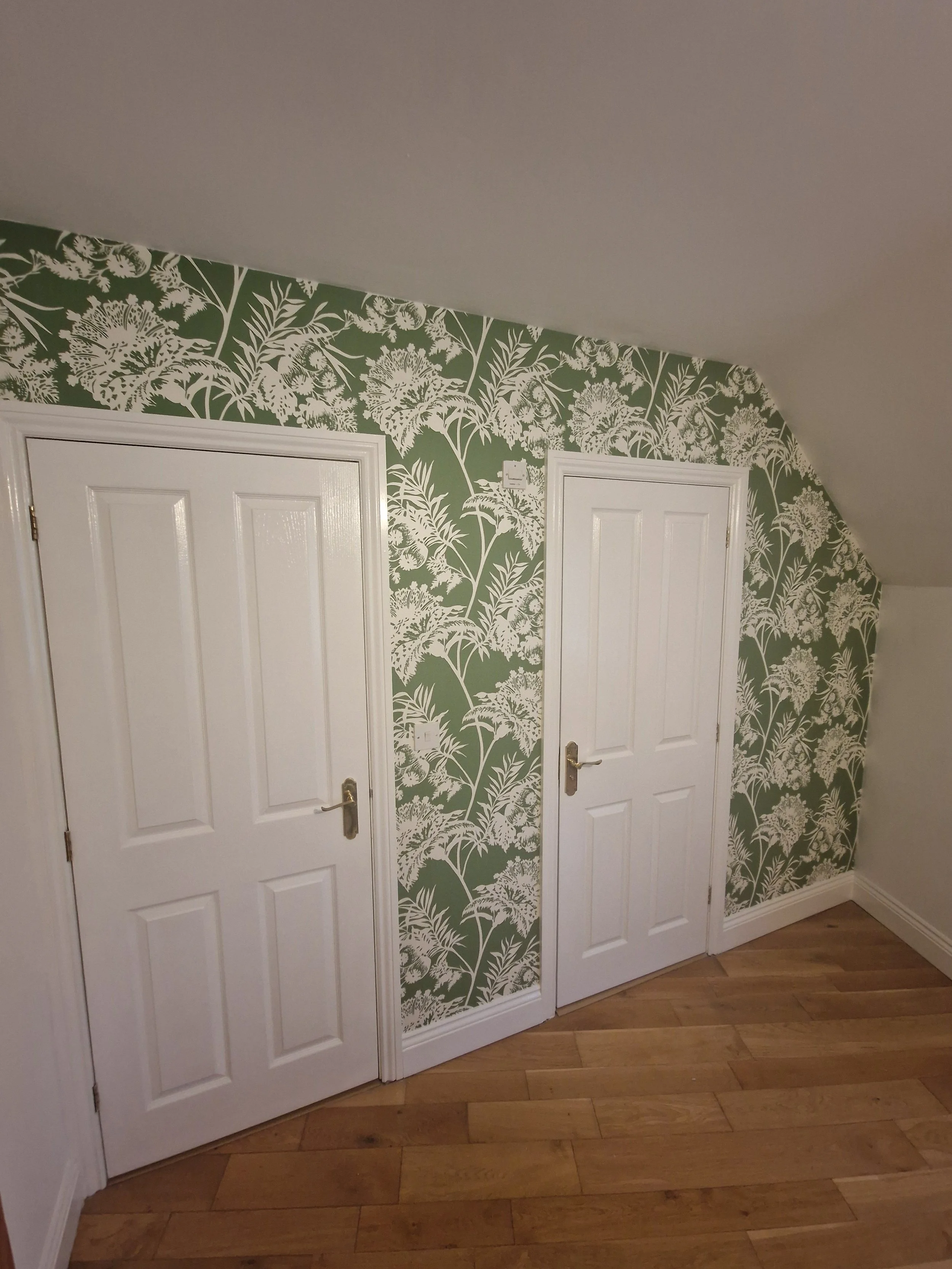 Pair of white interior doors in a room with green floral wallpaper and wooden flooring.
