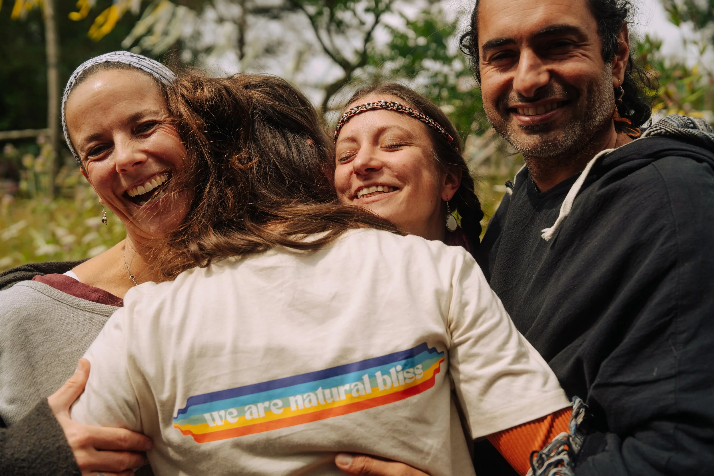 Vier Menschen umarmen sich freudig im Freien, lachend und glücklich, bei einem Treffen in der Natur.
