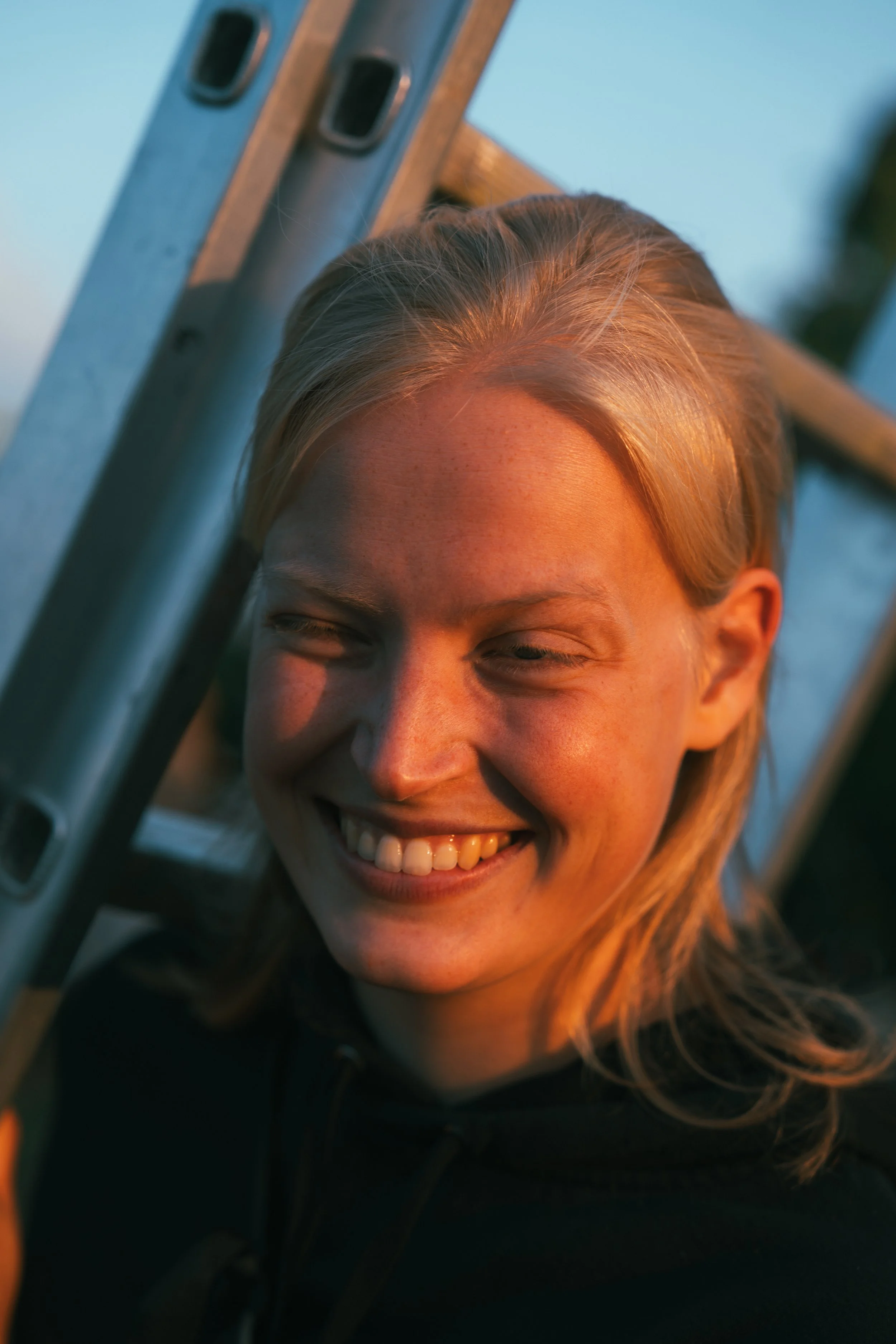 Humorvolle Frau lächelt während des Sonnenuntergangs neben einer Leiter.