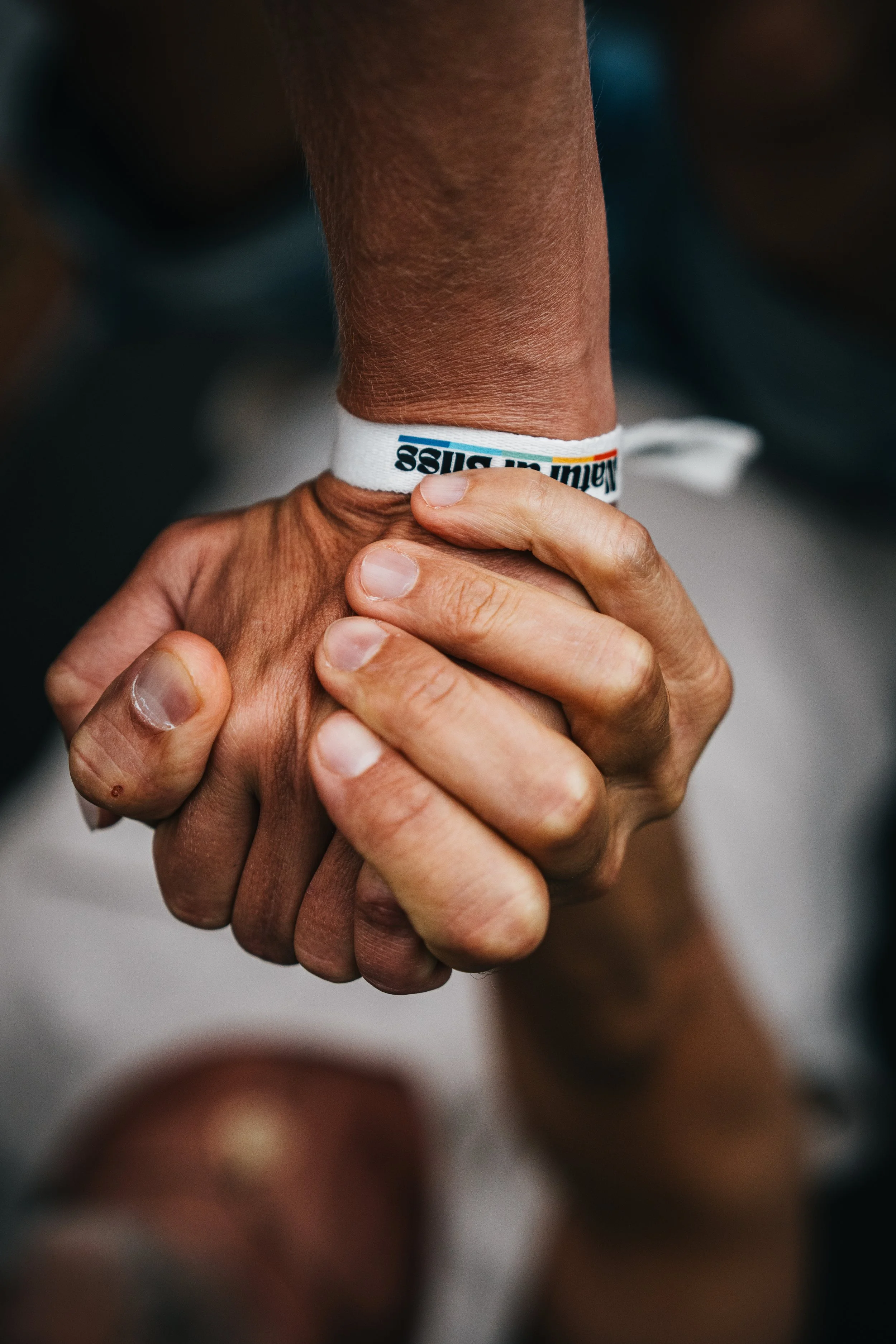 Nahaufnahme von zwei Händen, die sich festhalten, eine Person trägt ein weißes Armband mit Text.