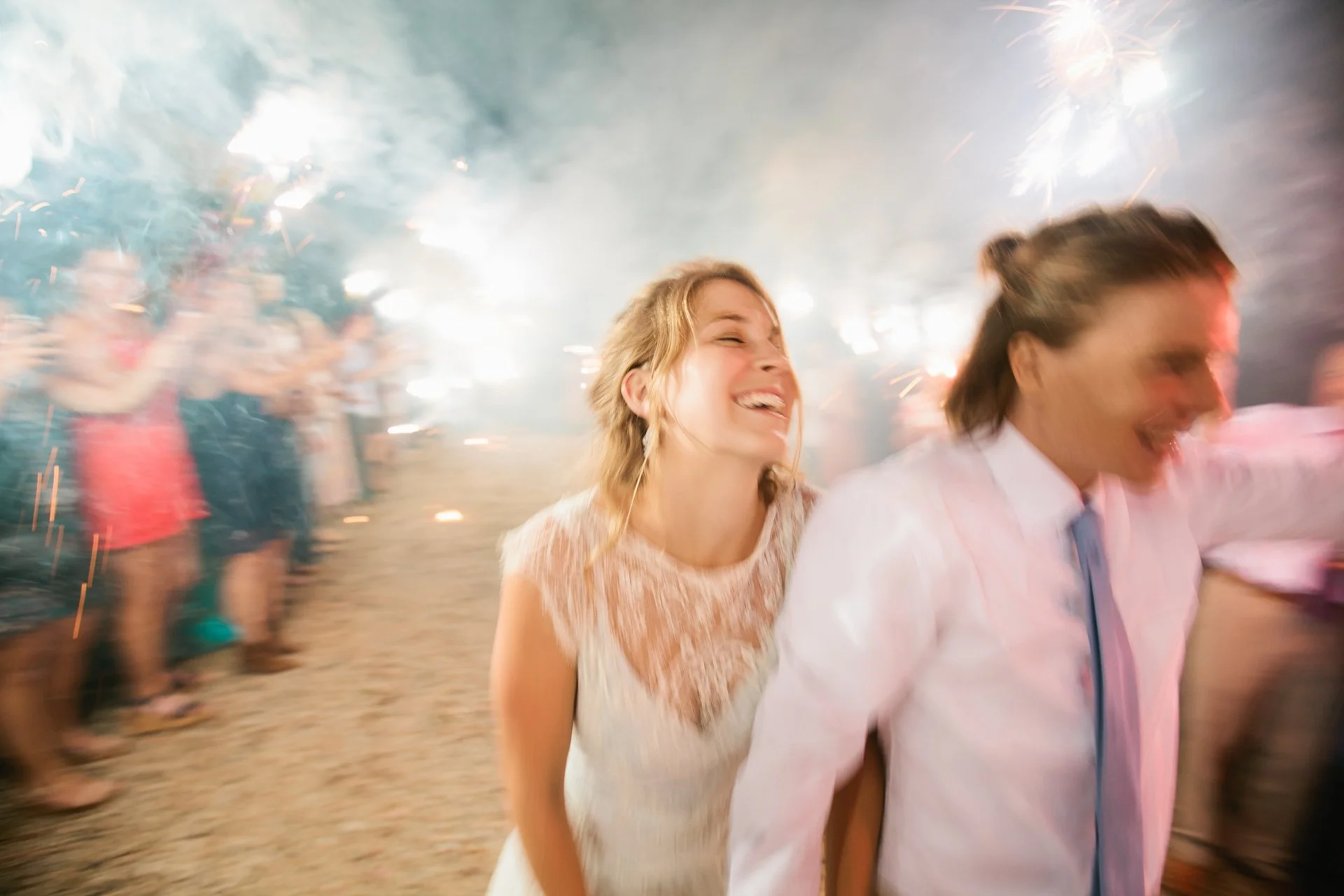 Two women laughing and dancing at a celebration with fireworks lighting up the background.
