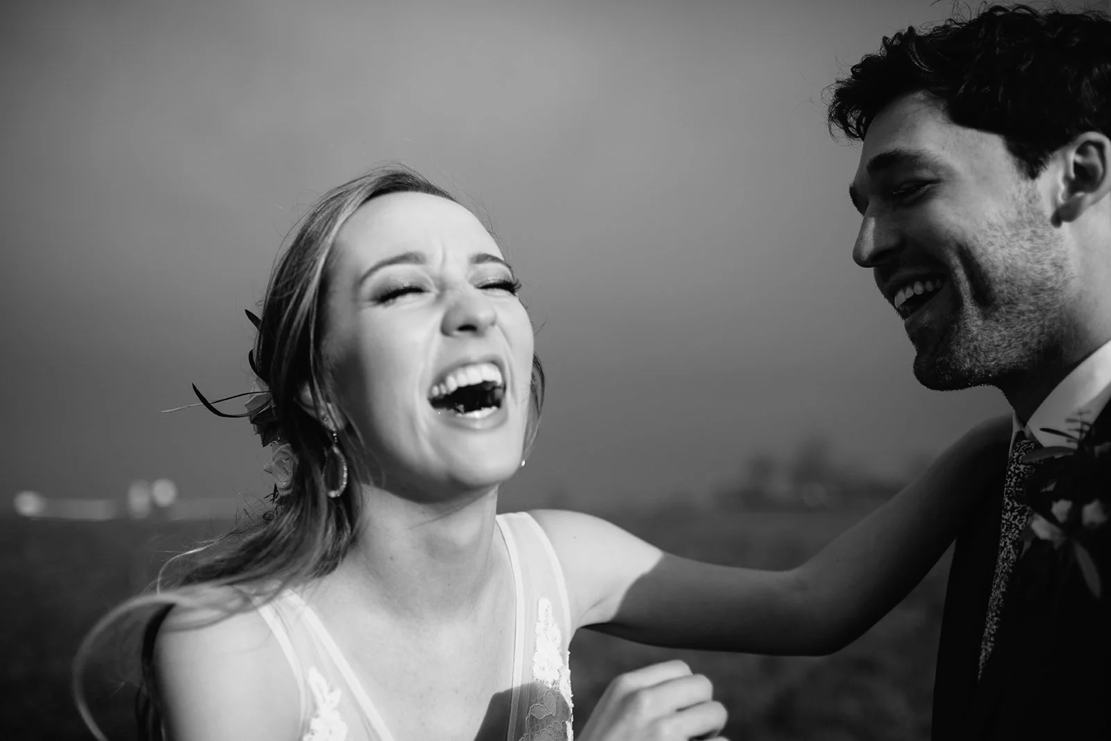 A black and white photo of a woman and a man smiling and laughing together outside, possibly at a wedding or celebration.