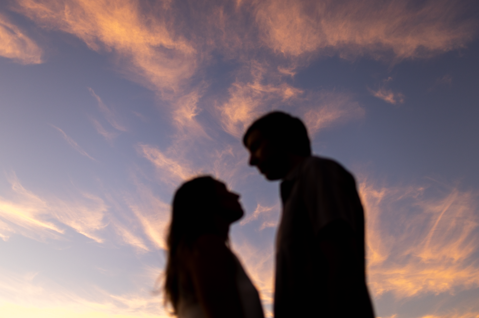Silhouette of a man and a woman looking at each other during sunset with a colorful sky and clouds in the background.