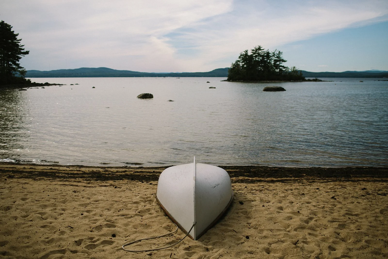 A white boat upside down on a sandy beach with water and an island in the background.