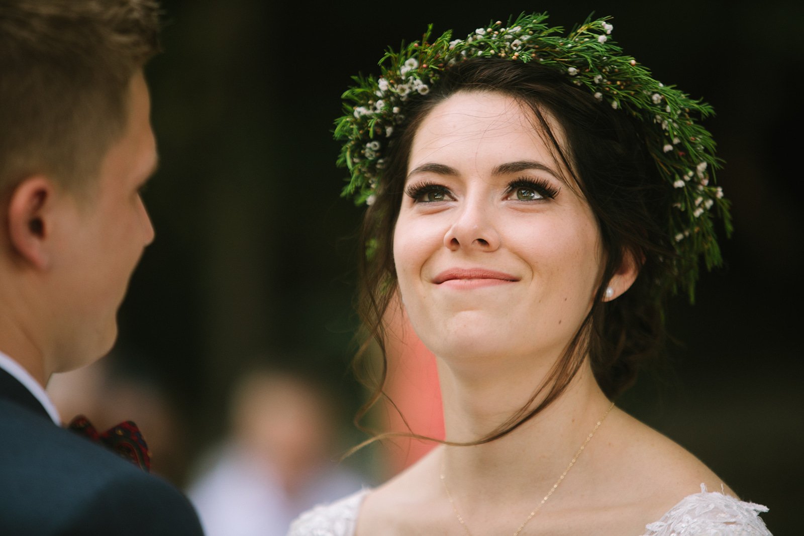 A woman wearing a floral crown gazes lovingly at a man during her wedding ceremony.