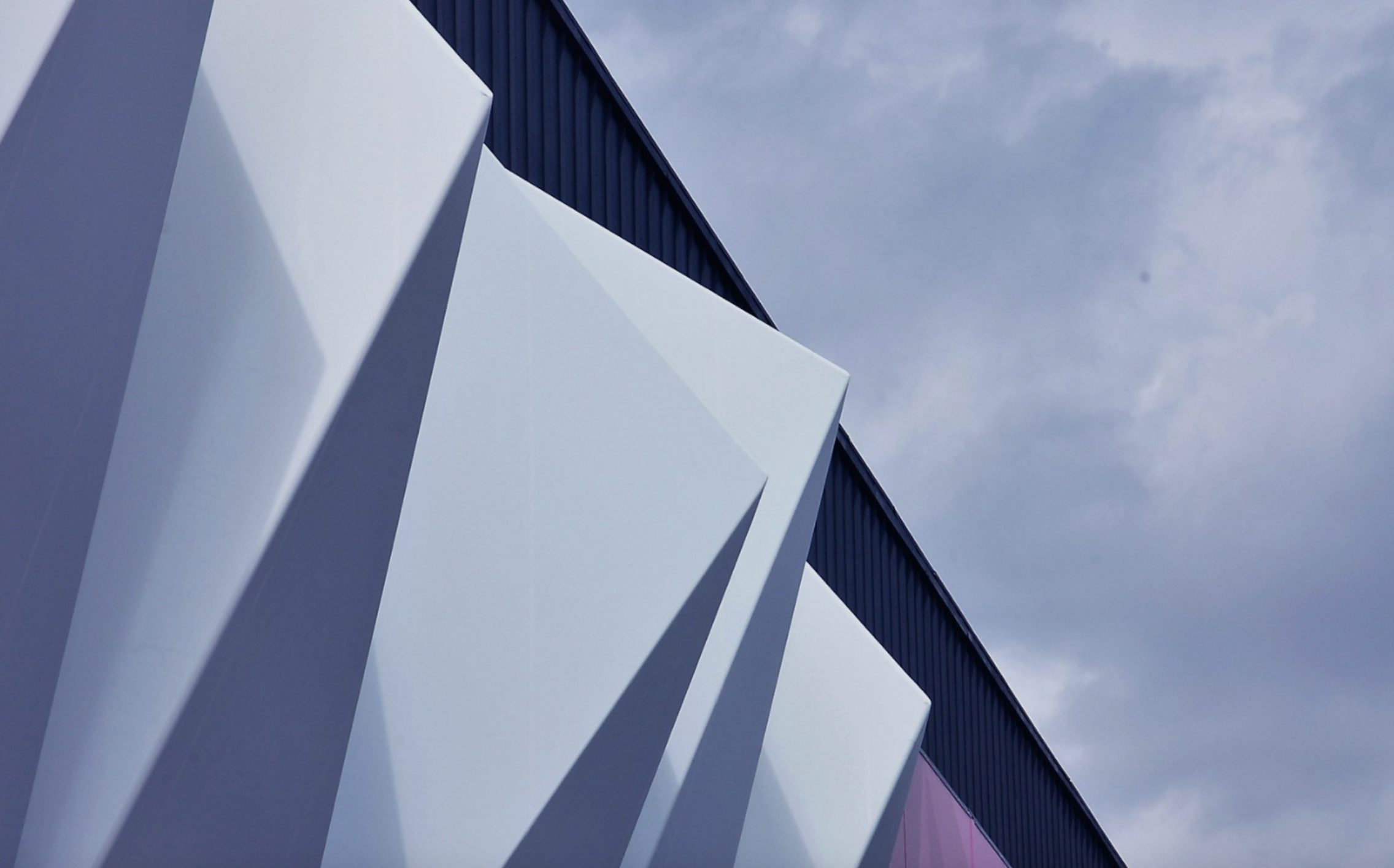 Close-up of modern building with blue, white, and purple panels under a cloudy sky.