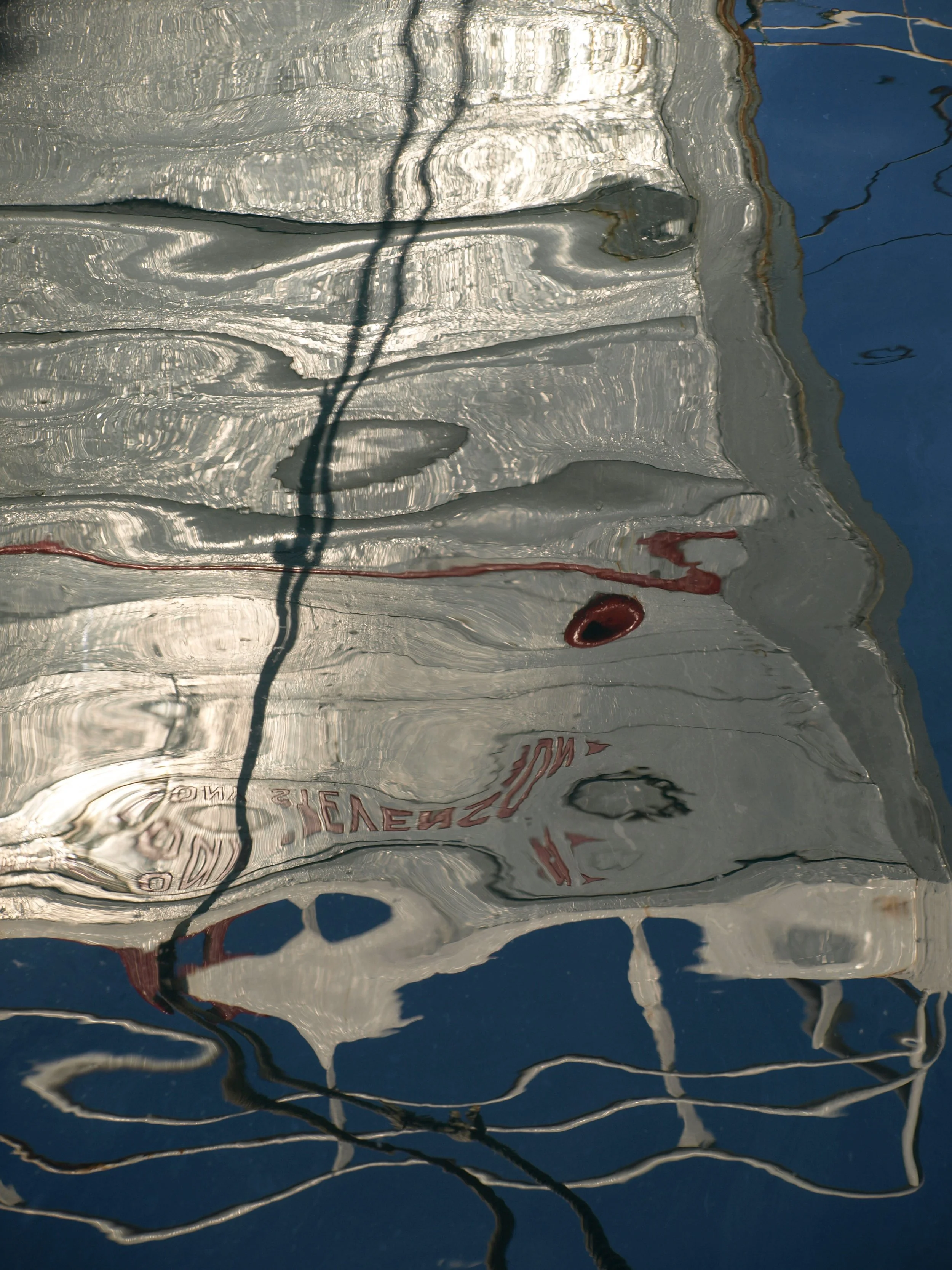 Reflection of a sign on the water with the words 'SHELTER' and other partially visible text, surrounded by ripples and shadows.